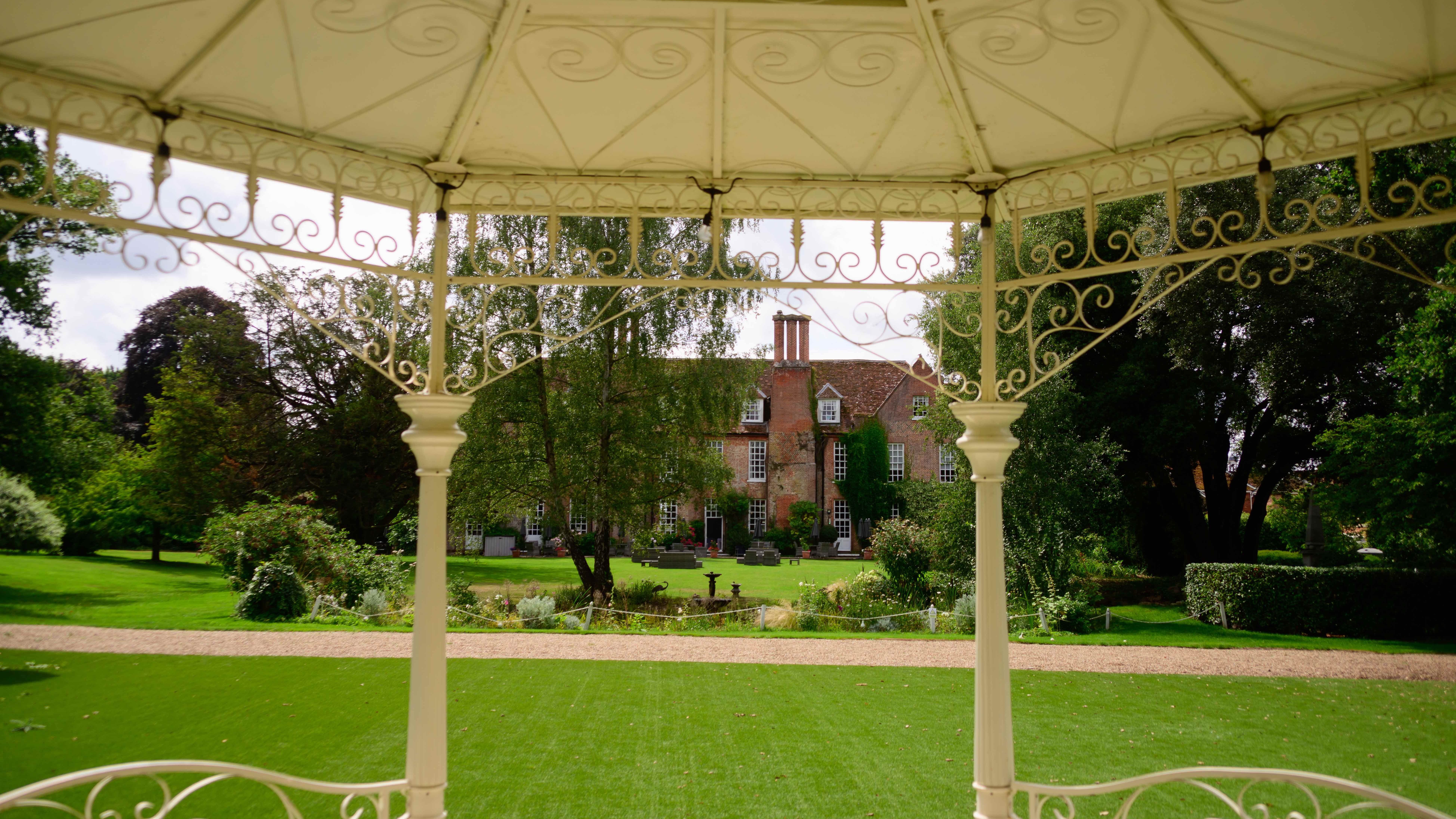 View from a gazebo looking onto a large garden with a historic brick mansion in the background.