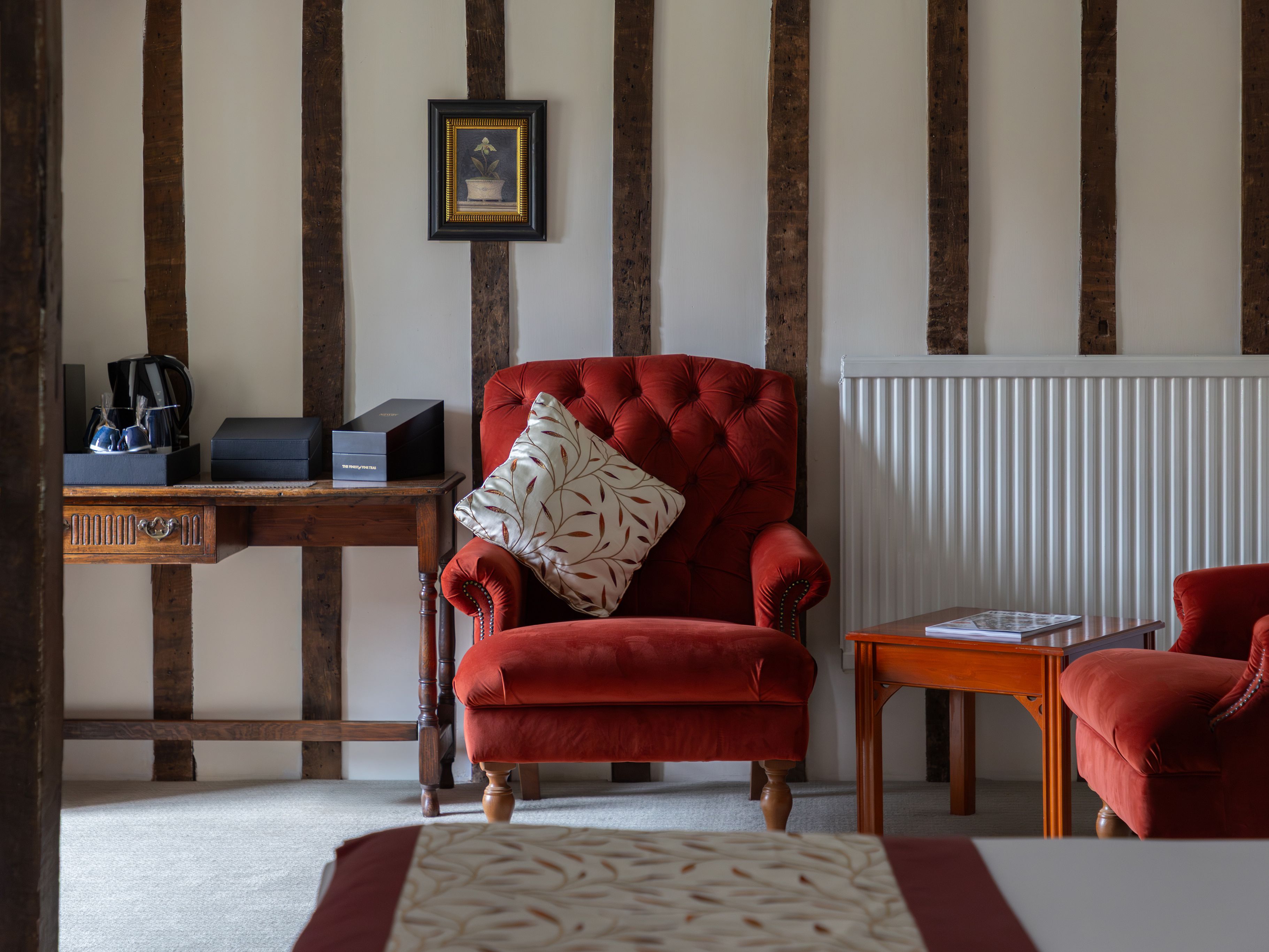 Cozy sitting area with red velvet armchairs, wooden table, and rustic exposed beams on the wall.