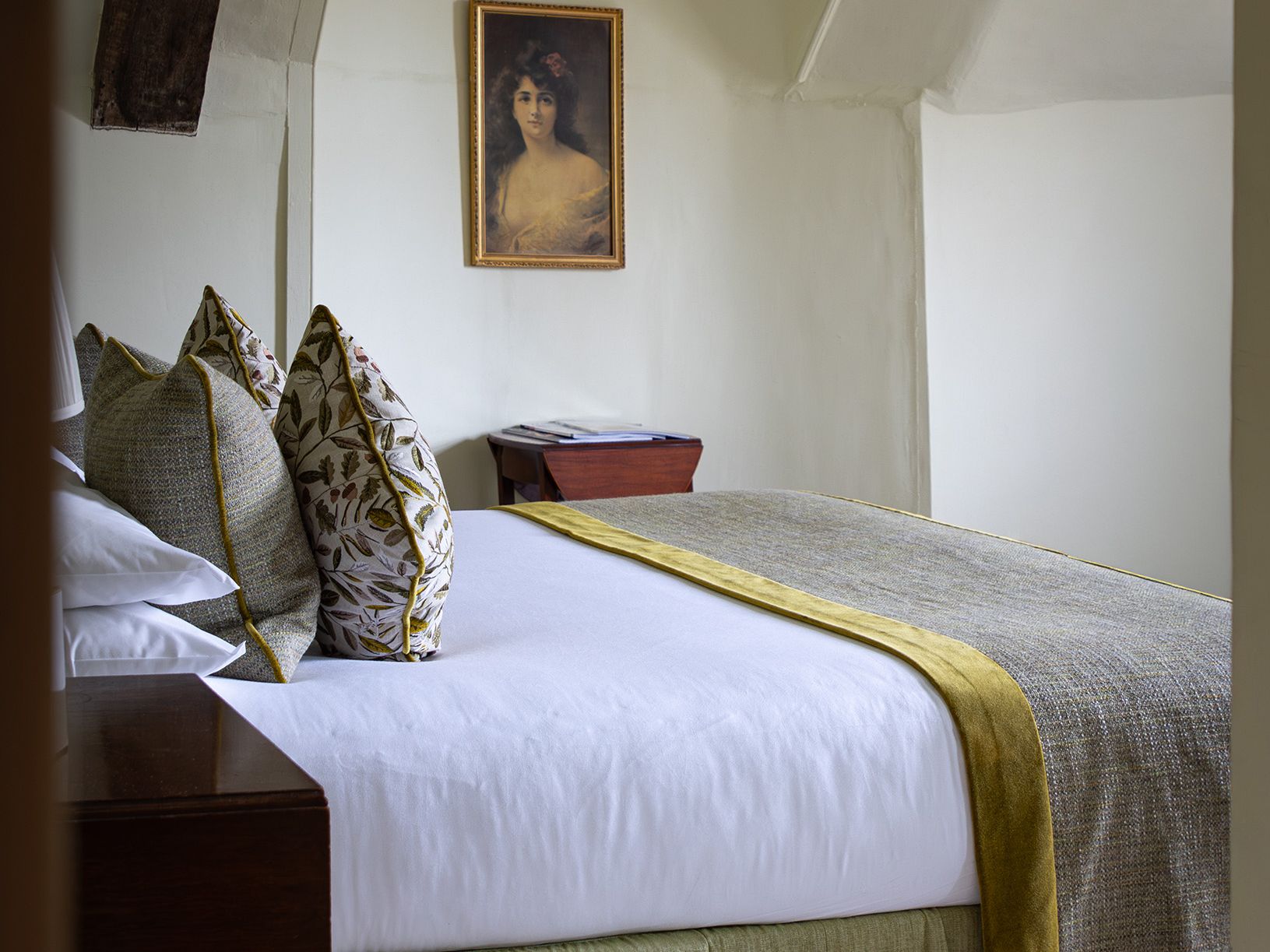 A neatly made bed with decorative pillows and a framed portrait of a woman hanging on the wall above a nightstand.