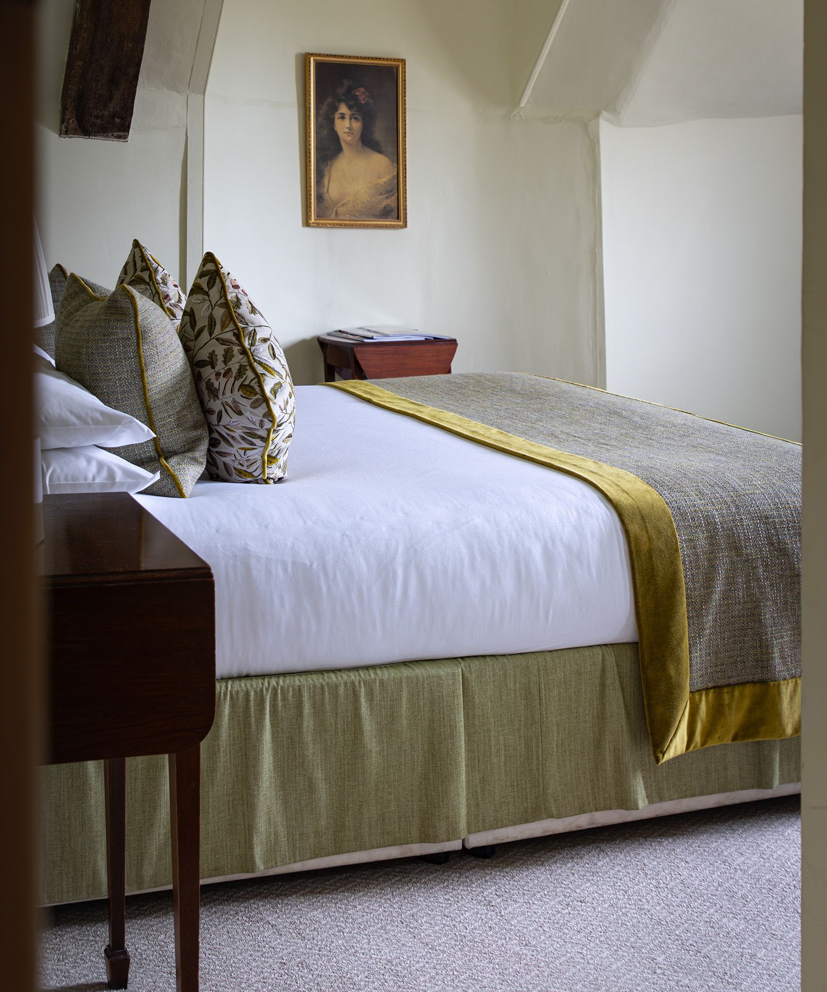 A neatly made bed with decorative pillows and a framed portrait of a woman hanging on the wall above a nightstand.
