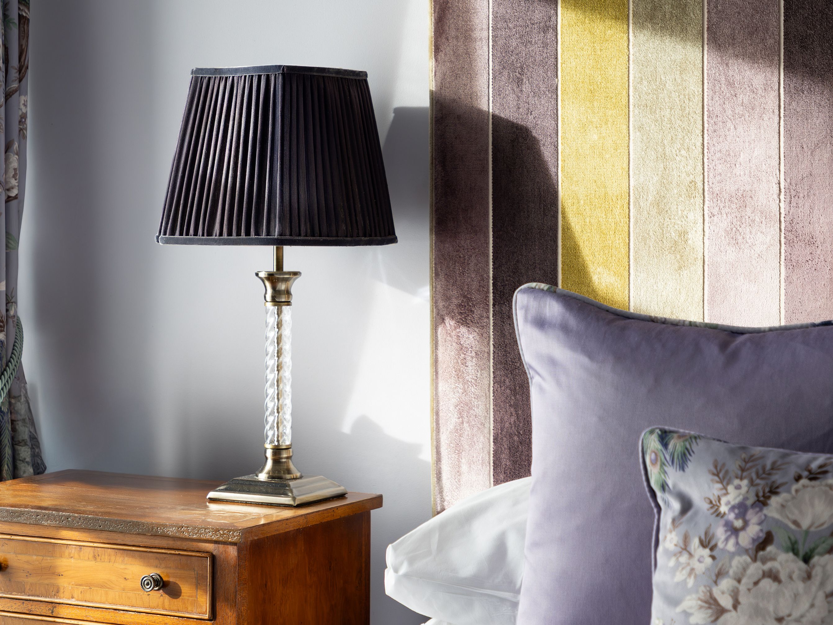 Bedside table with lamp, bed with striped headboard and decorative pillows