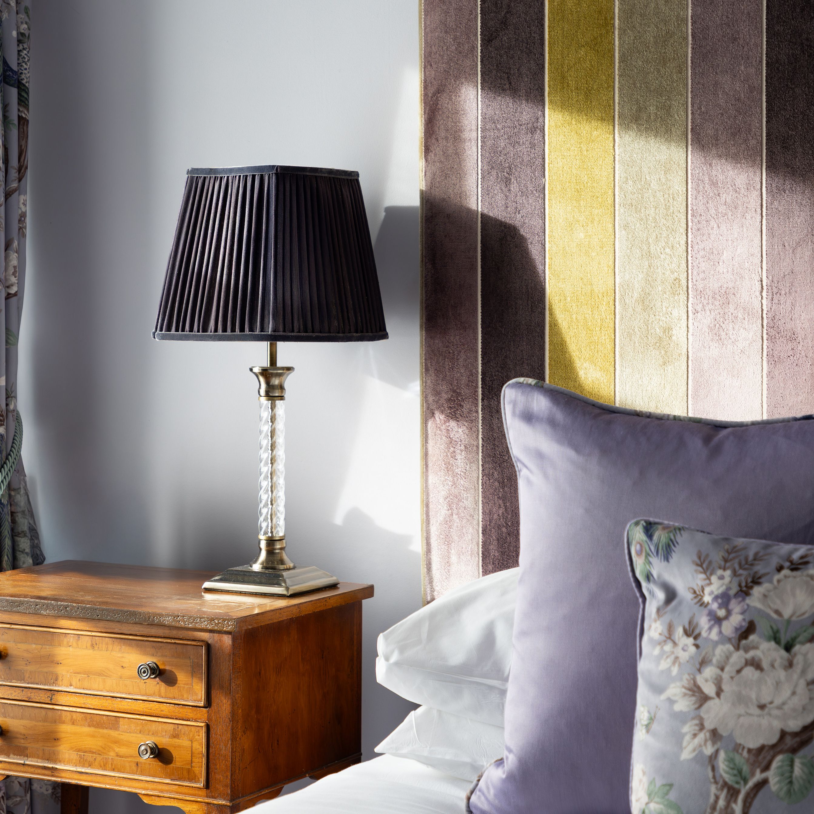 Bedside table with lamp, bed with striped headboard and decorative pillows