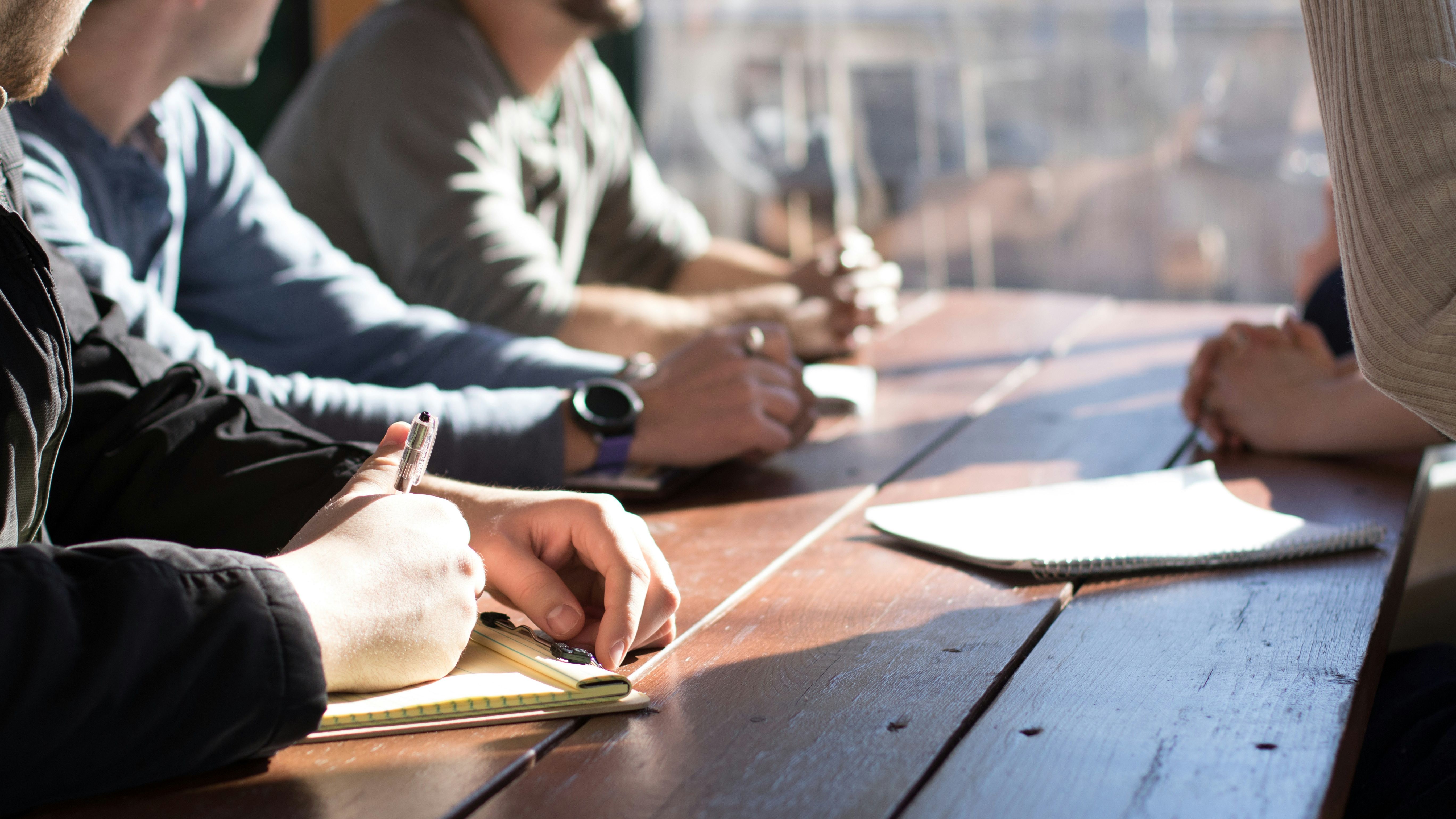 People sitting at a wooden table taking notes during a meeting.