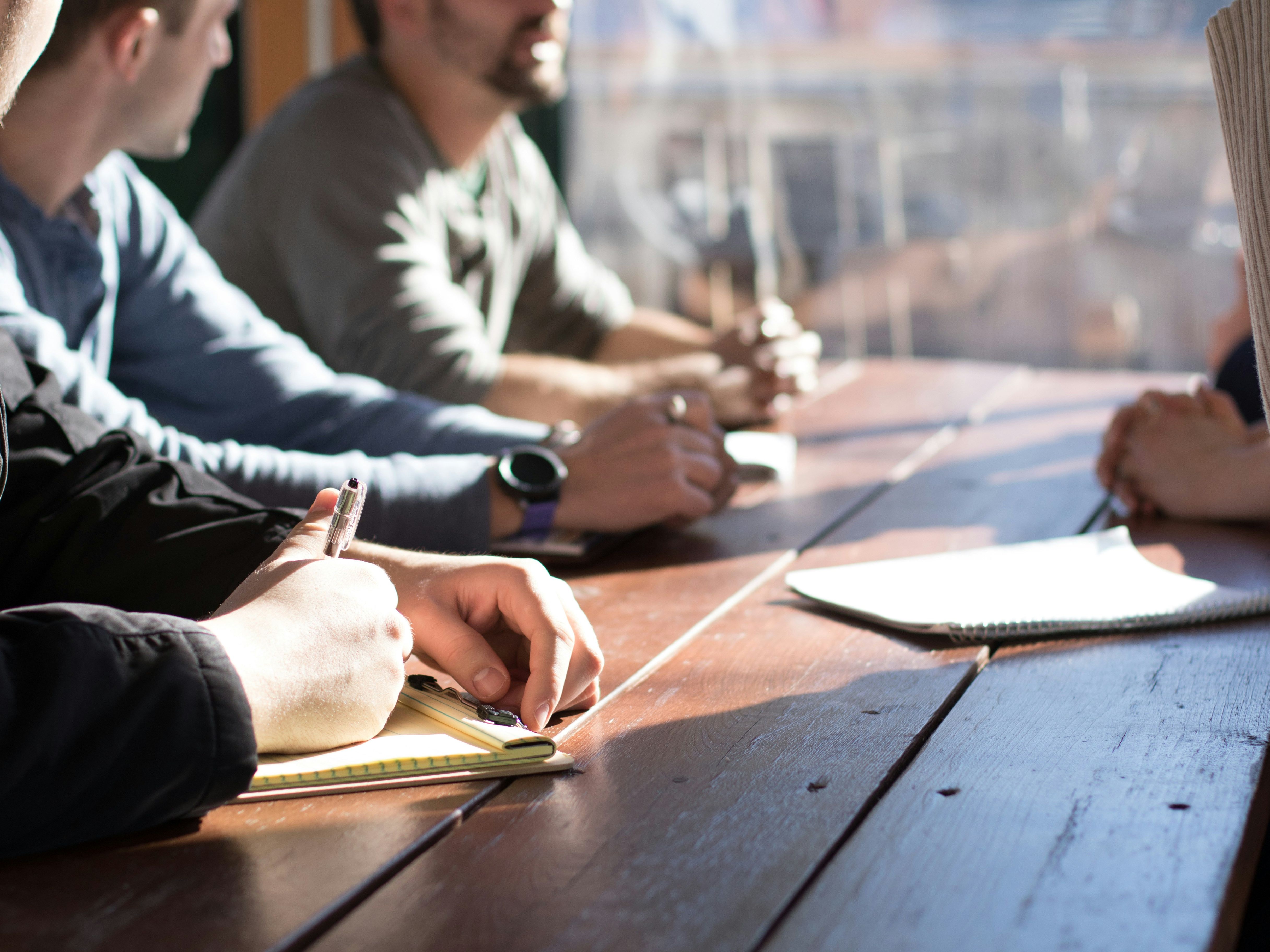People sitting at a wooden table taking notes during a meeting.