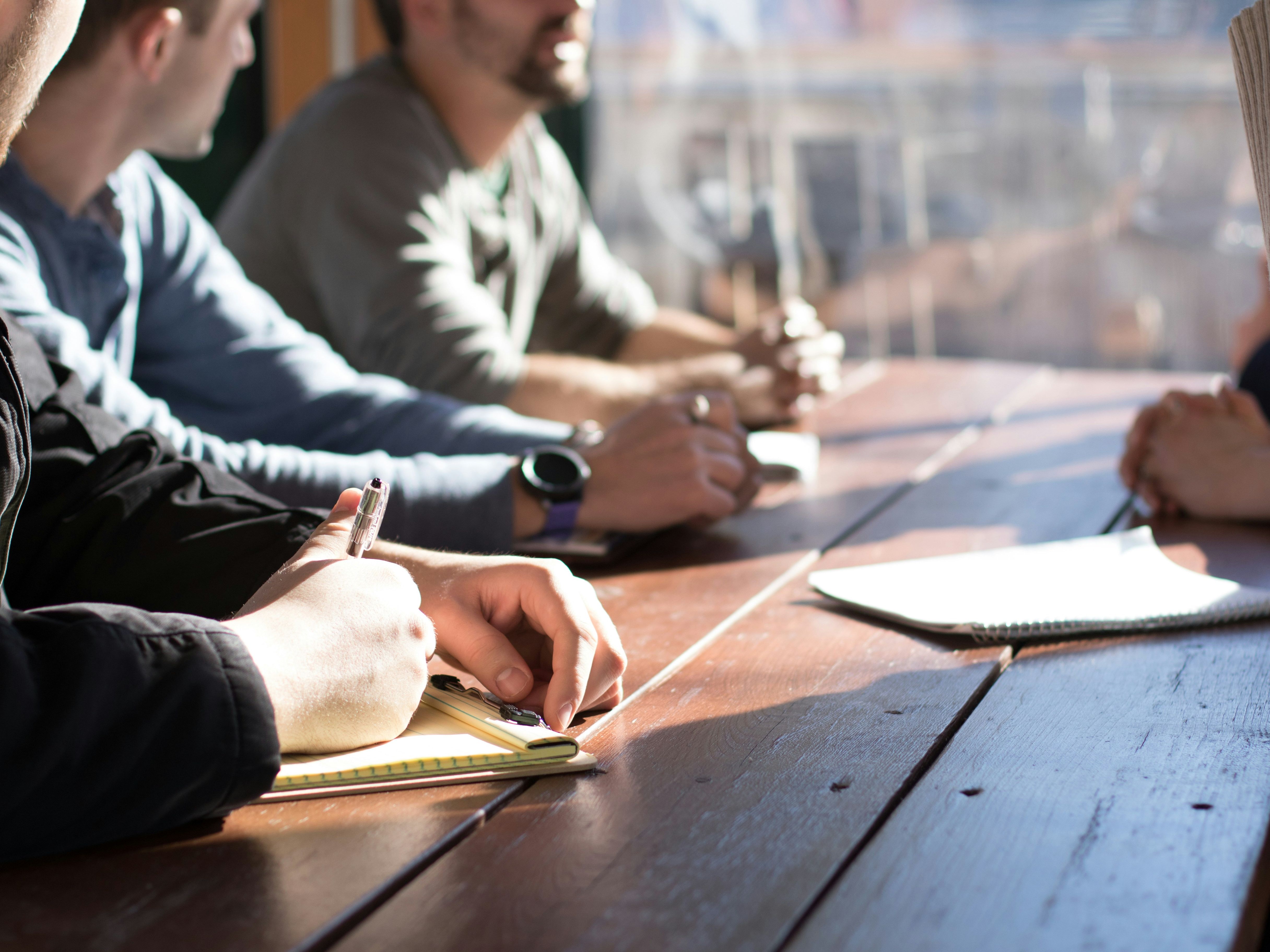 People sitting at a wooden table taking notes during a meeting.