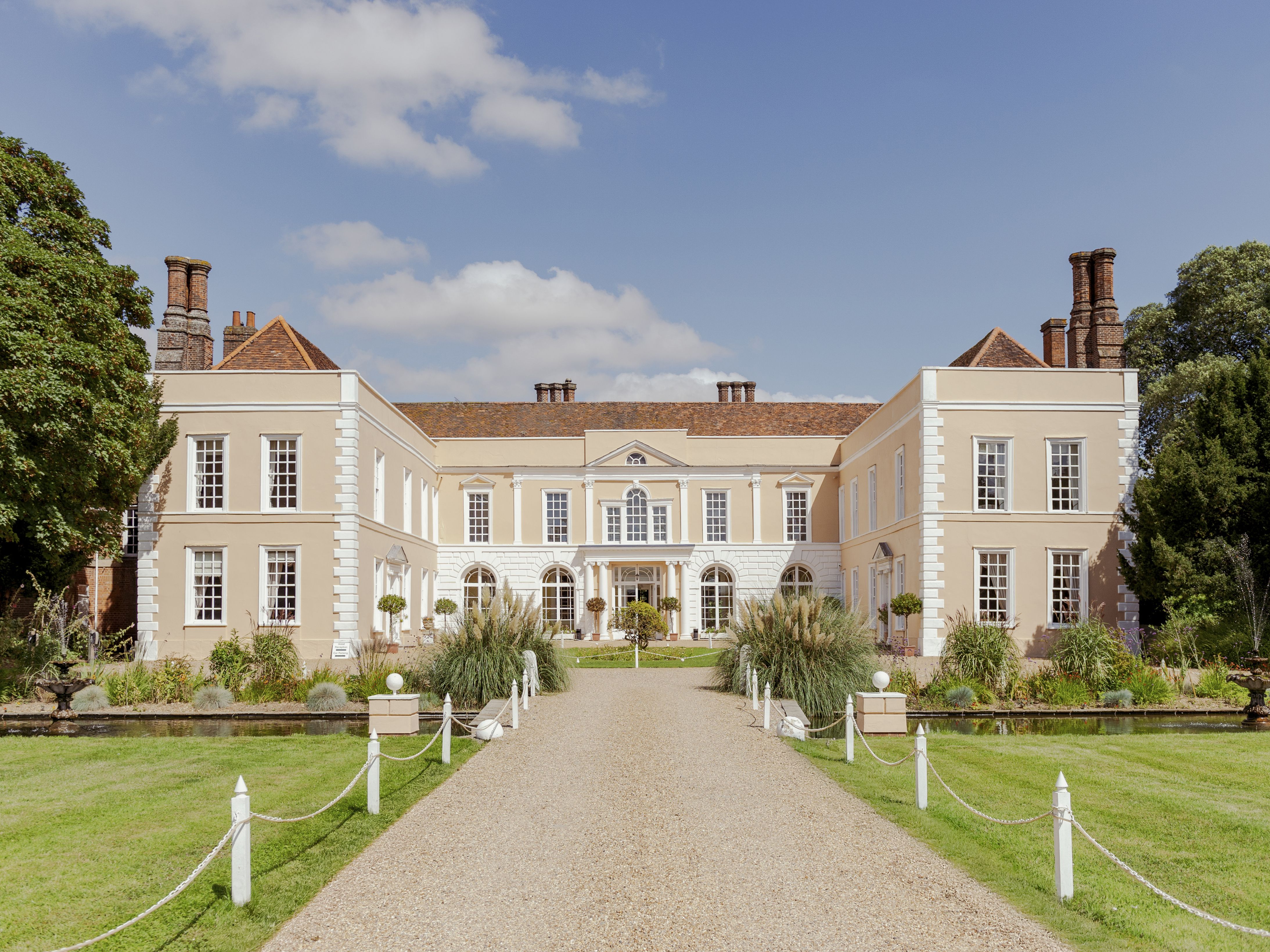 Large stately manor house with symmetrical architecture, gardens, and a gravel driveway