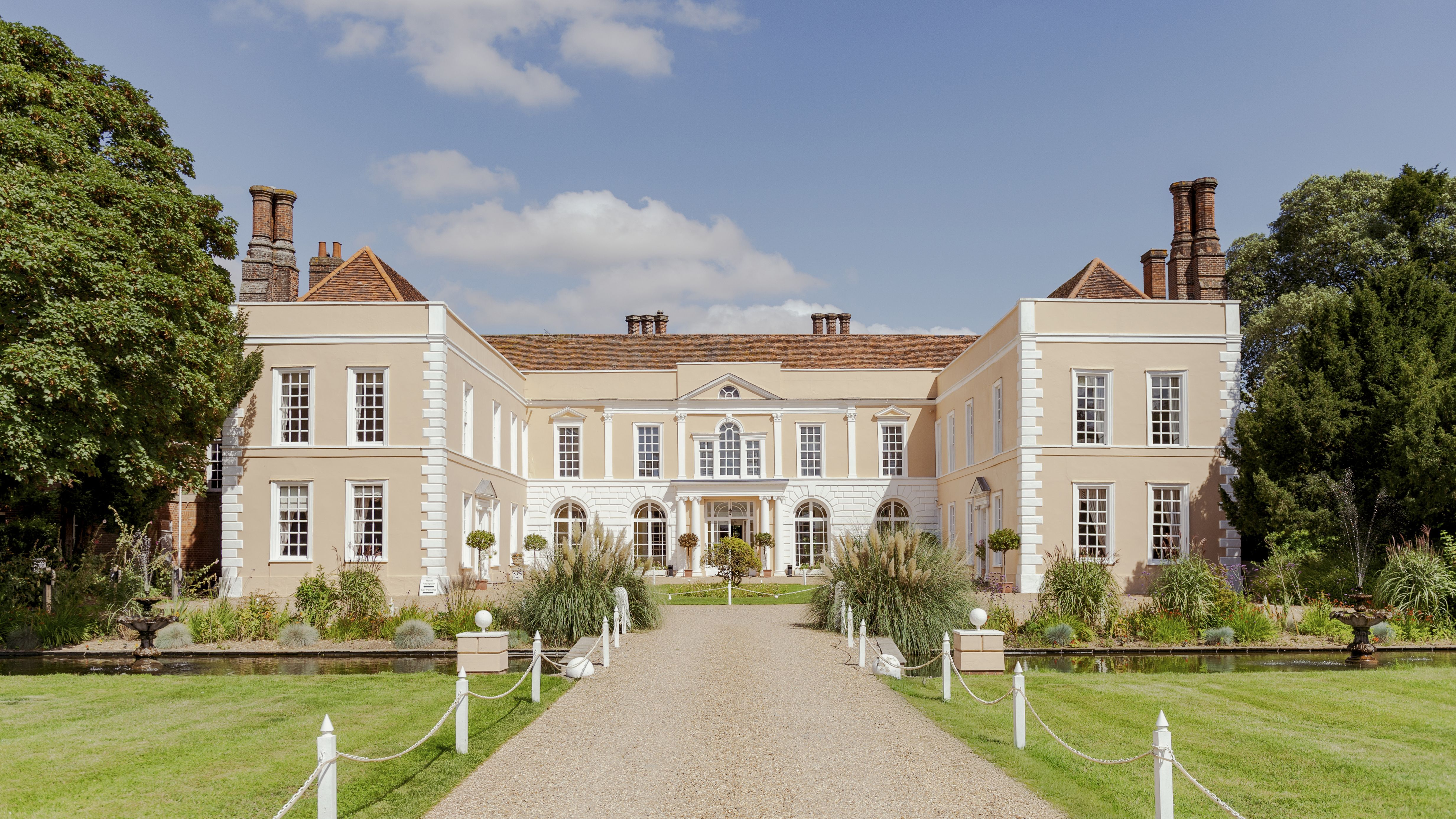 Large stately manor house with symmetrical architecture, gardens, and a gravel driveway