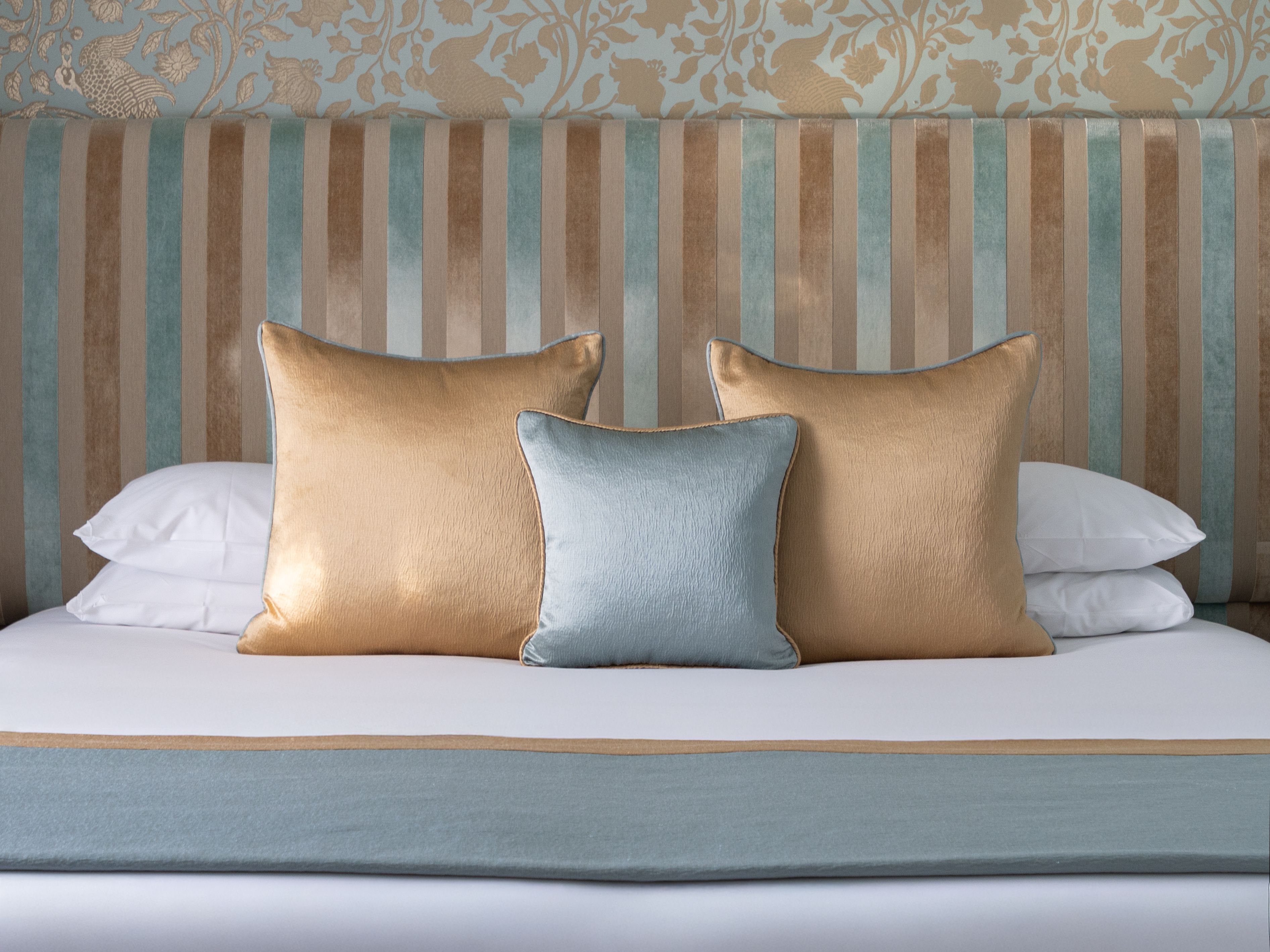 Elegant bed with gold and blue pillows against a decorative wall
