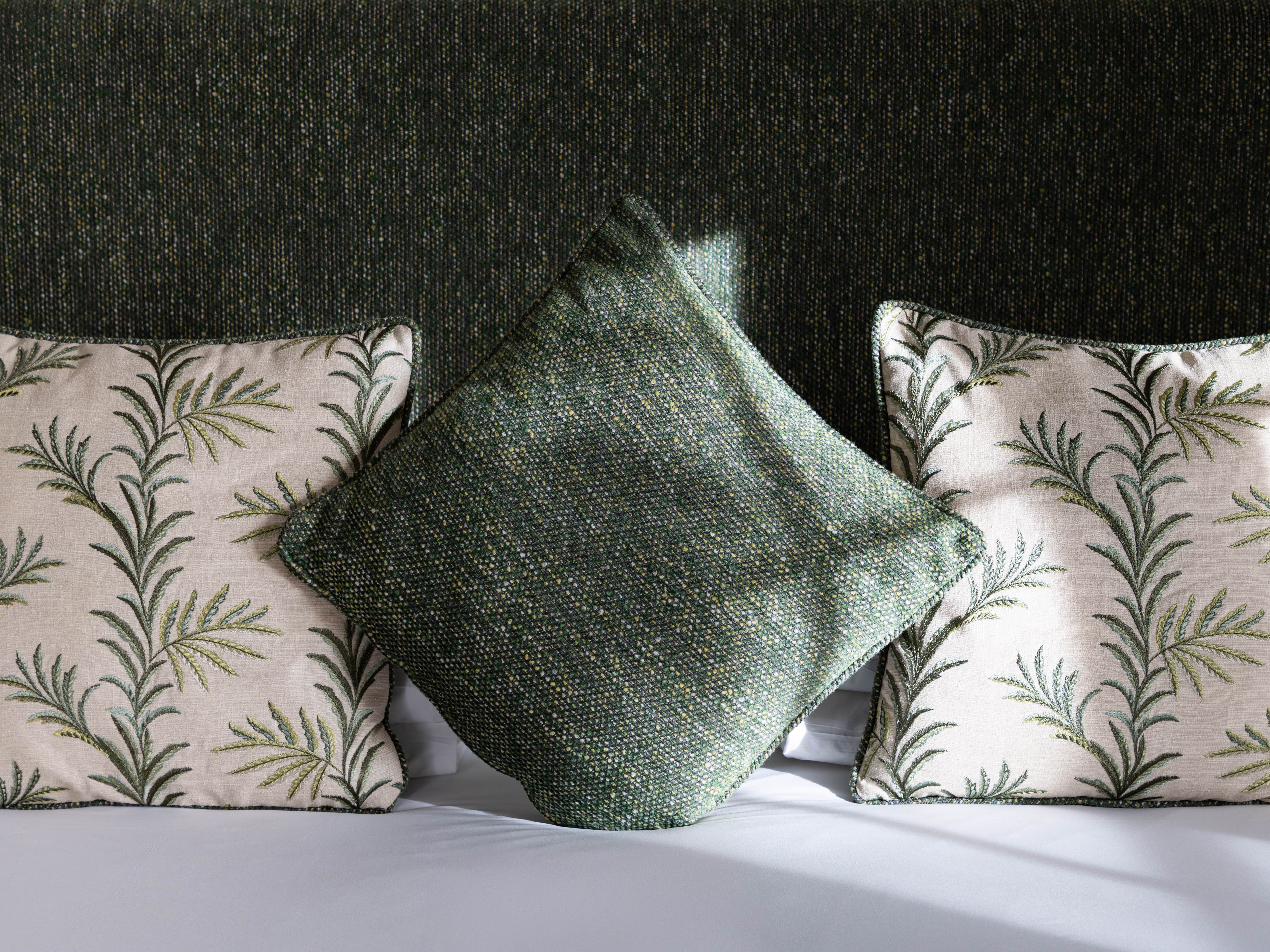 Three decorative pillows on a bed, two with leaf patterns and one plain green pillow