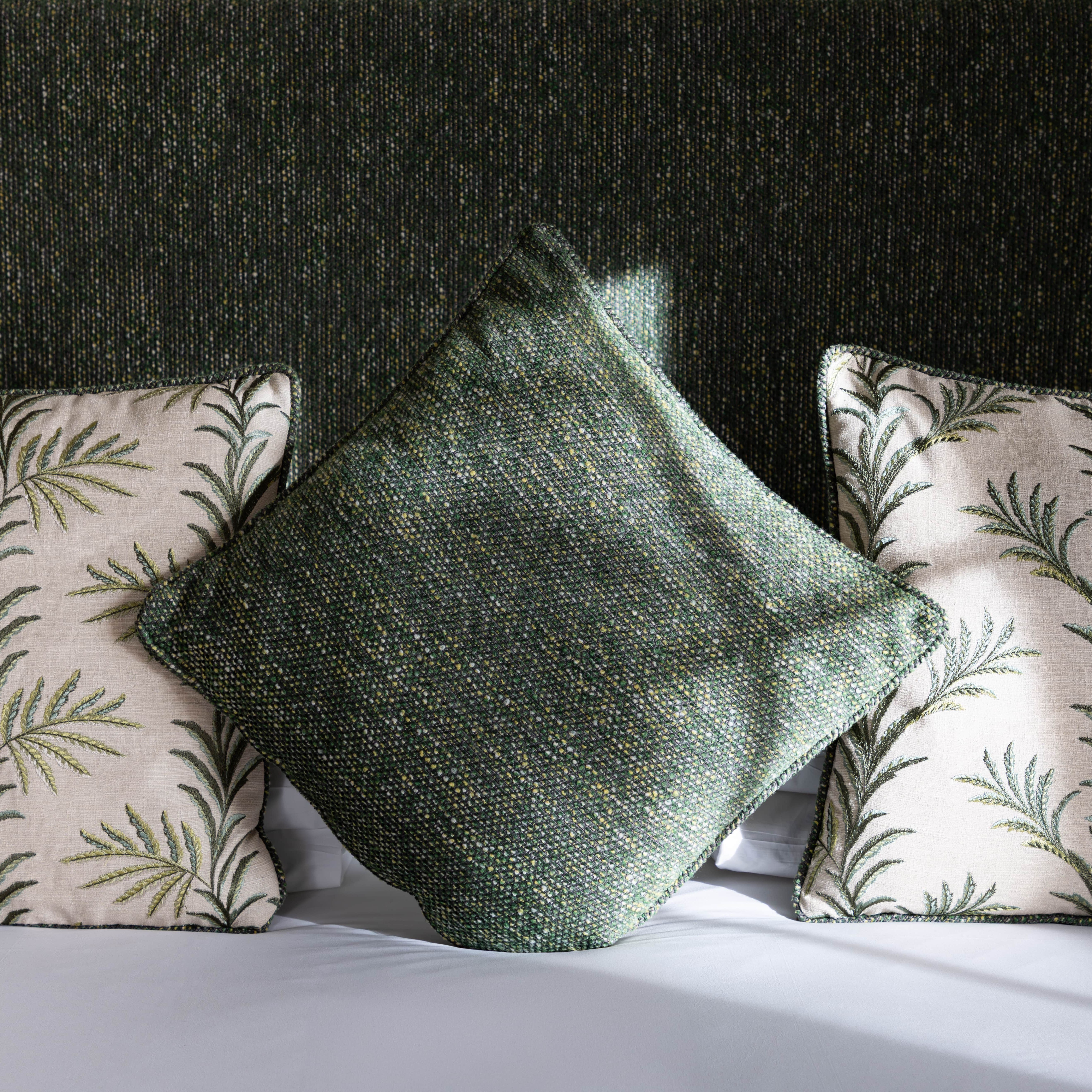 Three decorative pillows on a bed, two with leaf patterns and one plain green pillow