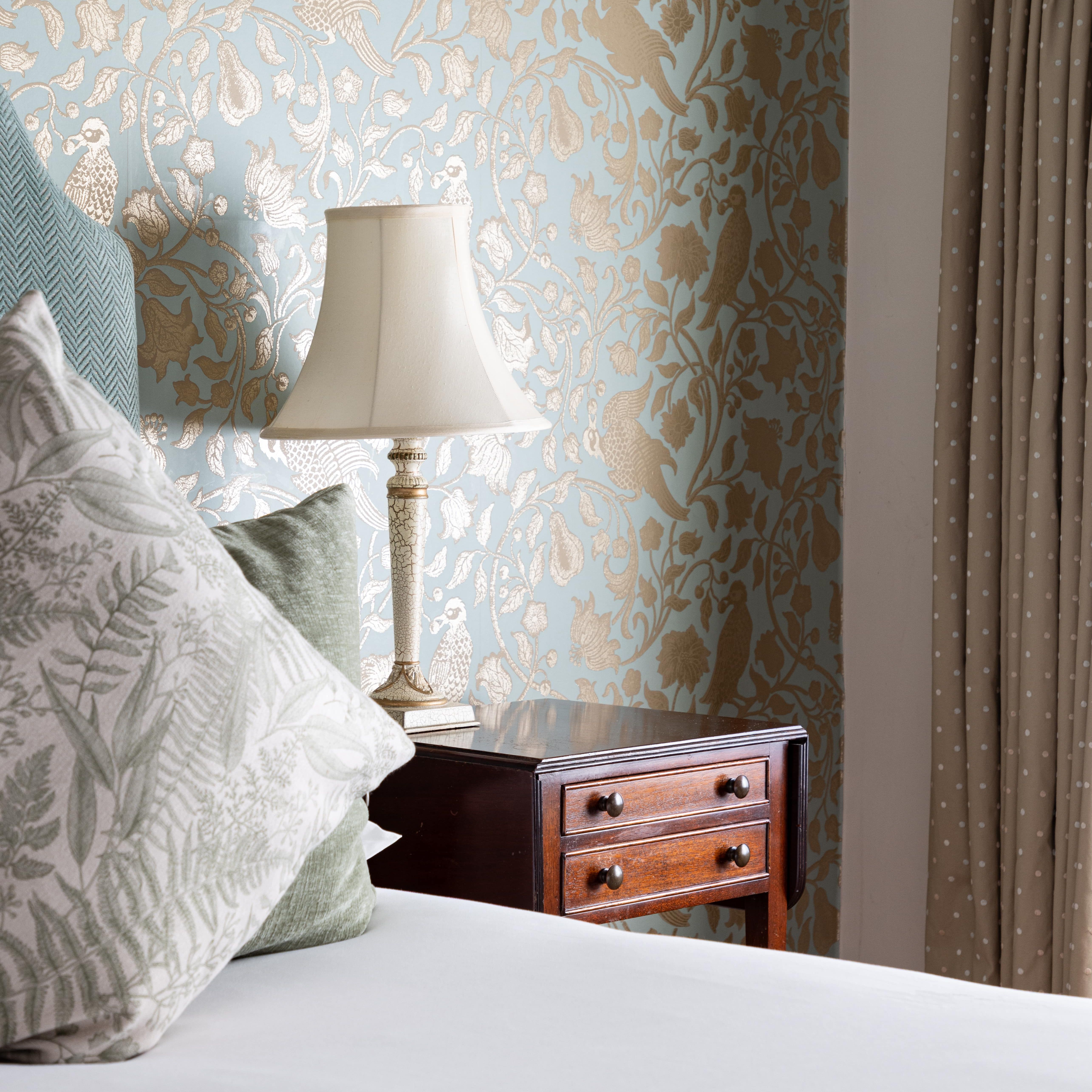 Bedroom corner with patterned wallpaper, bedside table, lamp, and pillows