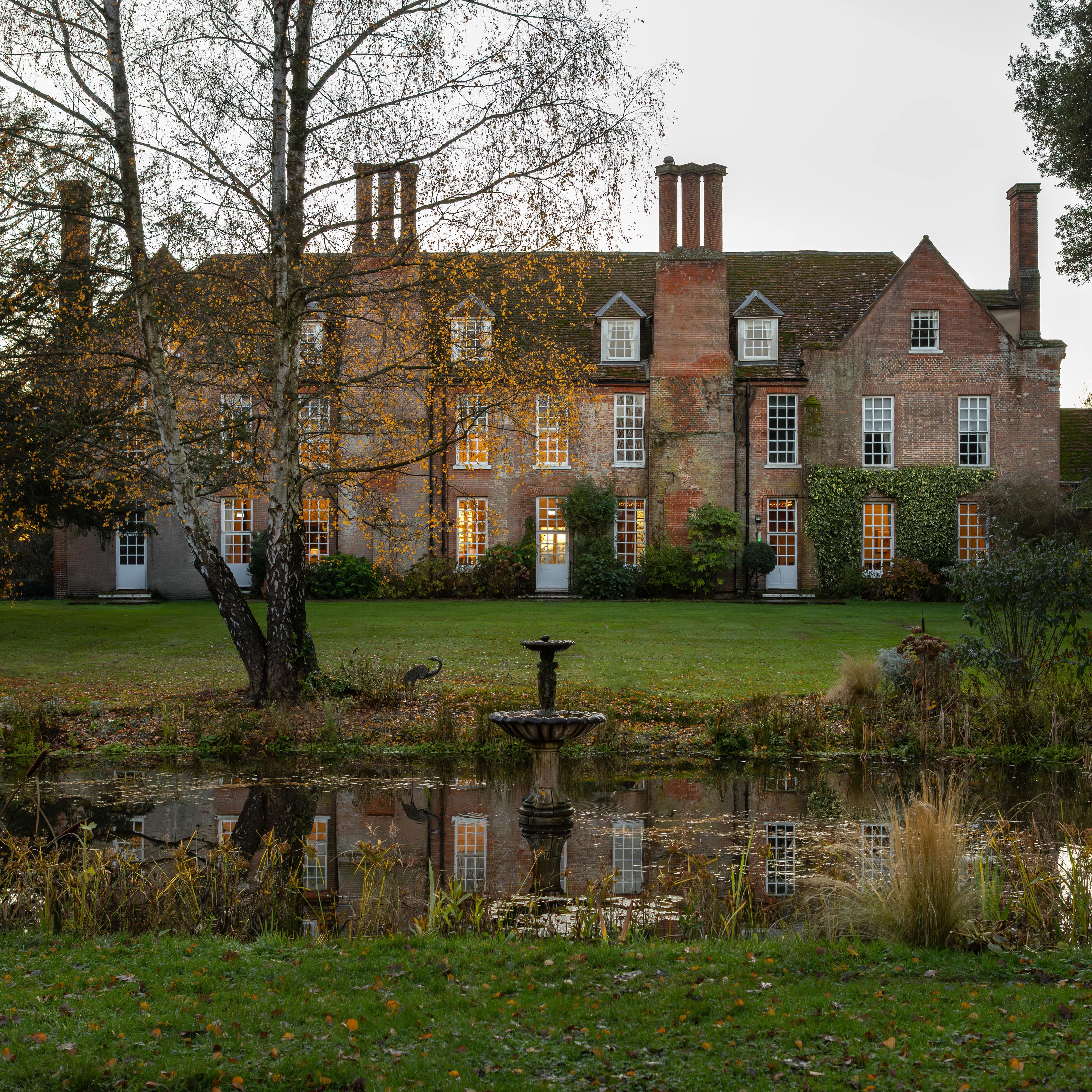 Large historic brick manor house with many chimneys, surrounded by a garden and a pond in front