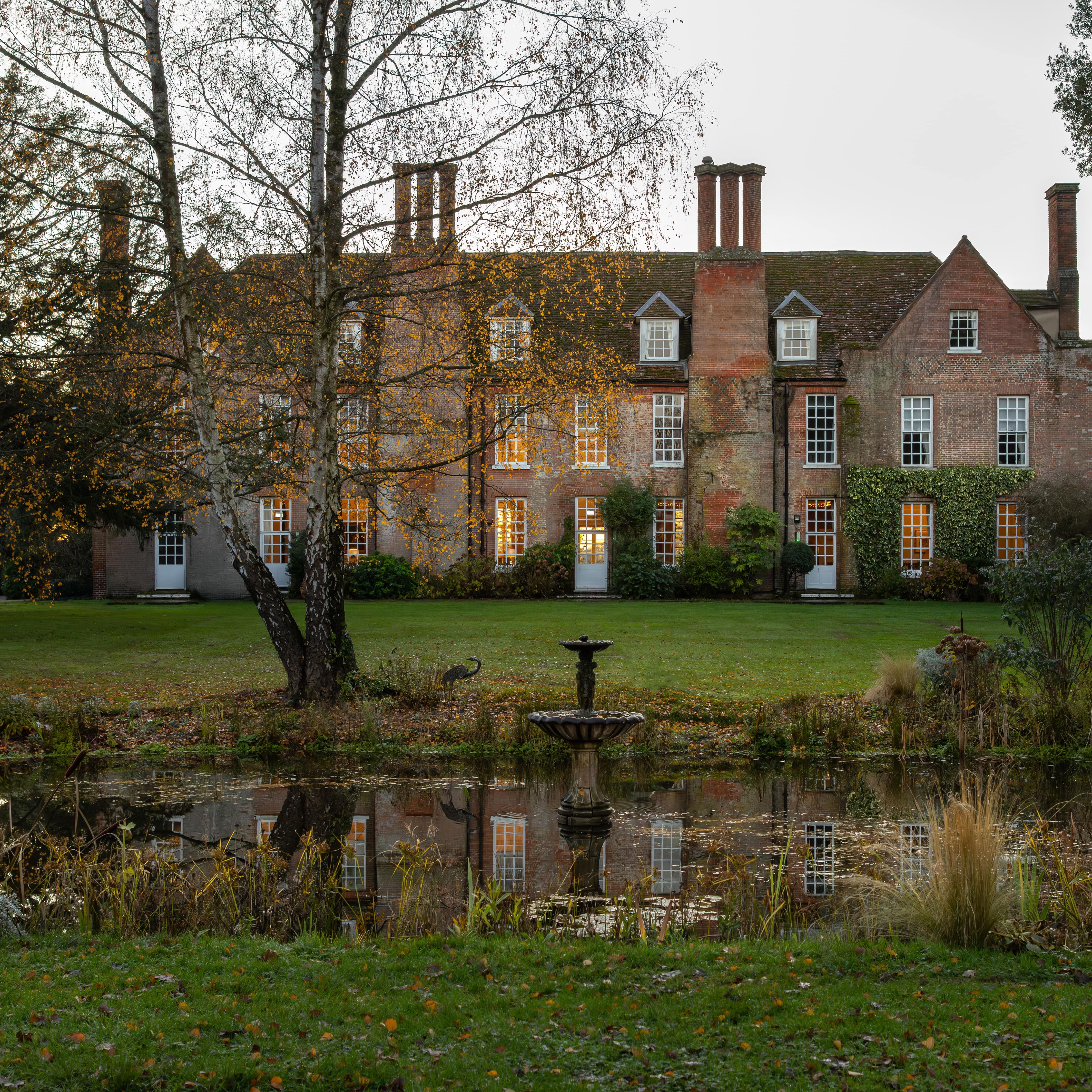 Large historic brick manor house with many chimneys, surrounded by a garden and a pond in front