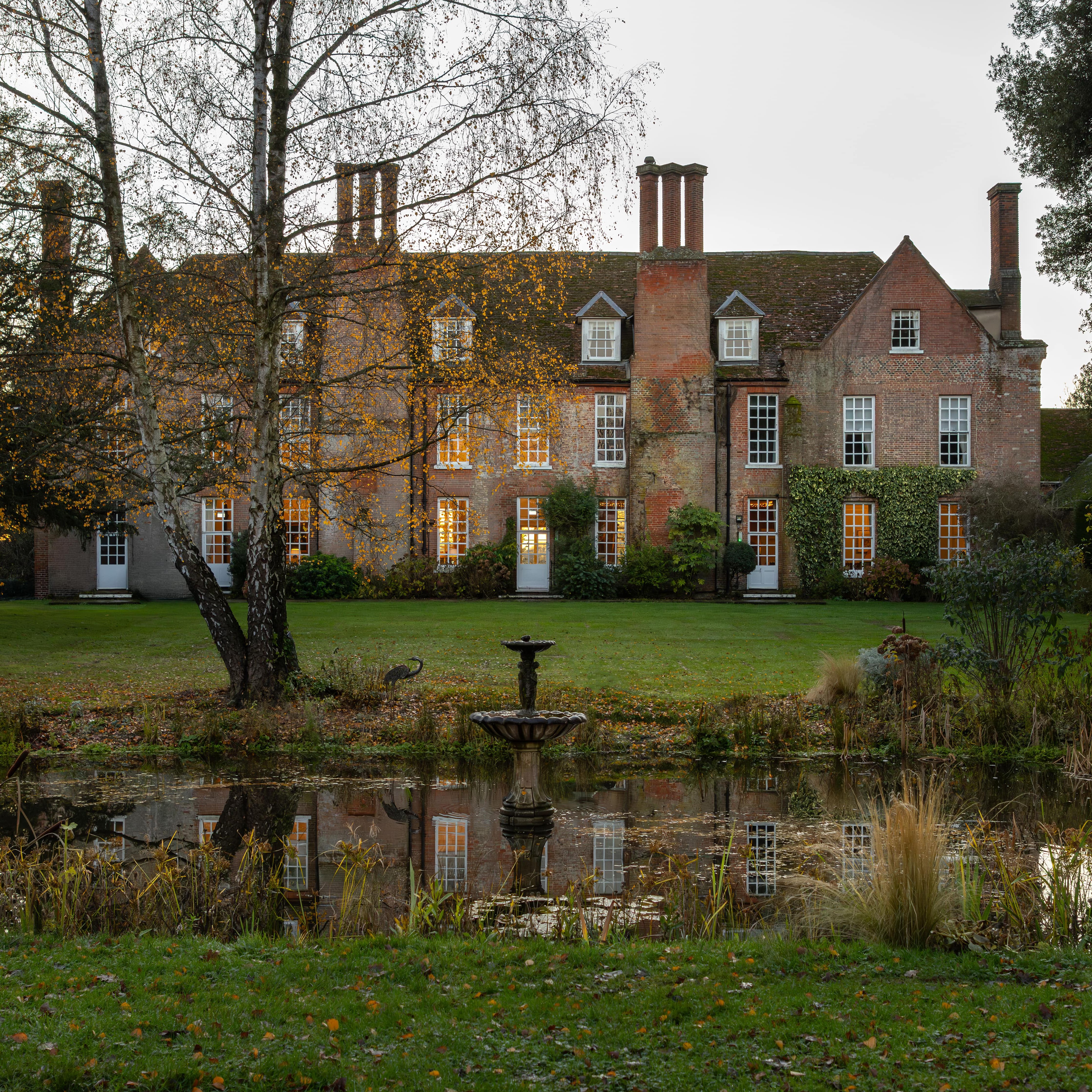 Large historic brick manor house with many chimneys, surrounded by a garden and a pond in front