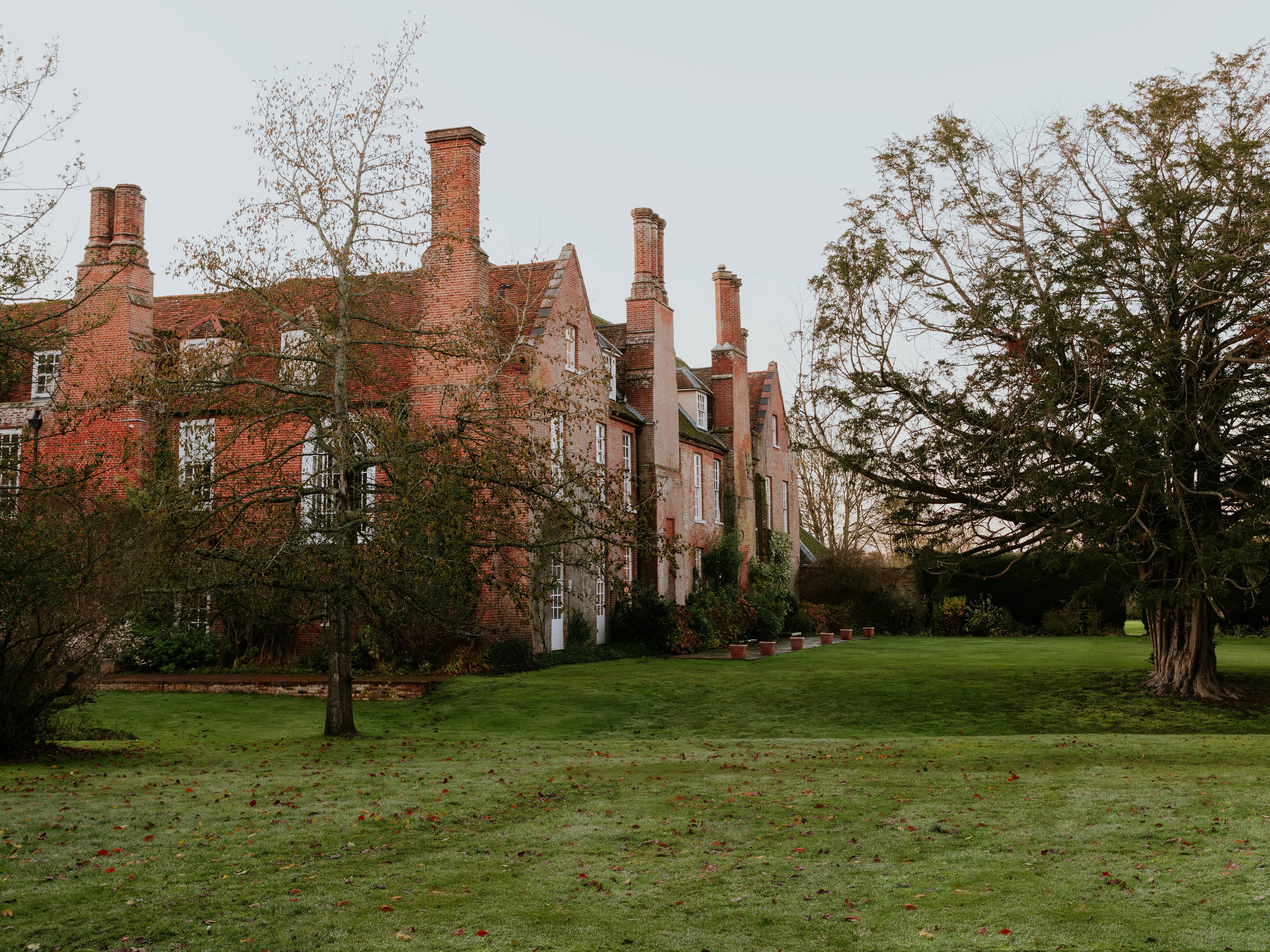 Large historic brick house with multiple chimneys surrounded by trees and a grassy lawn.