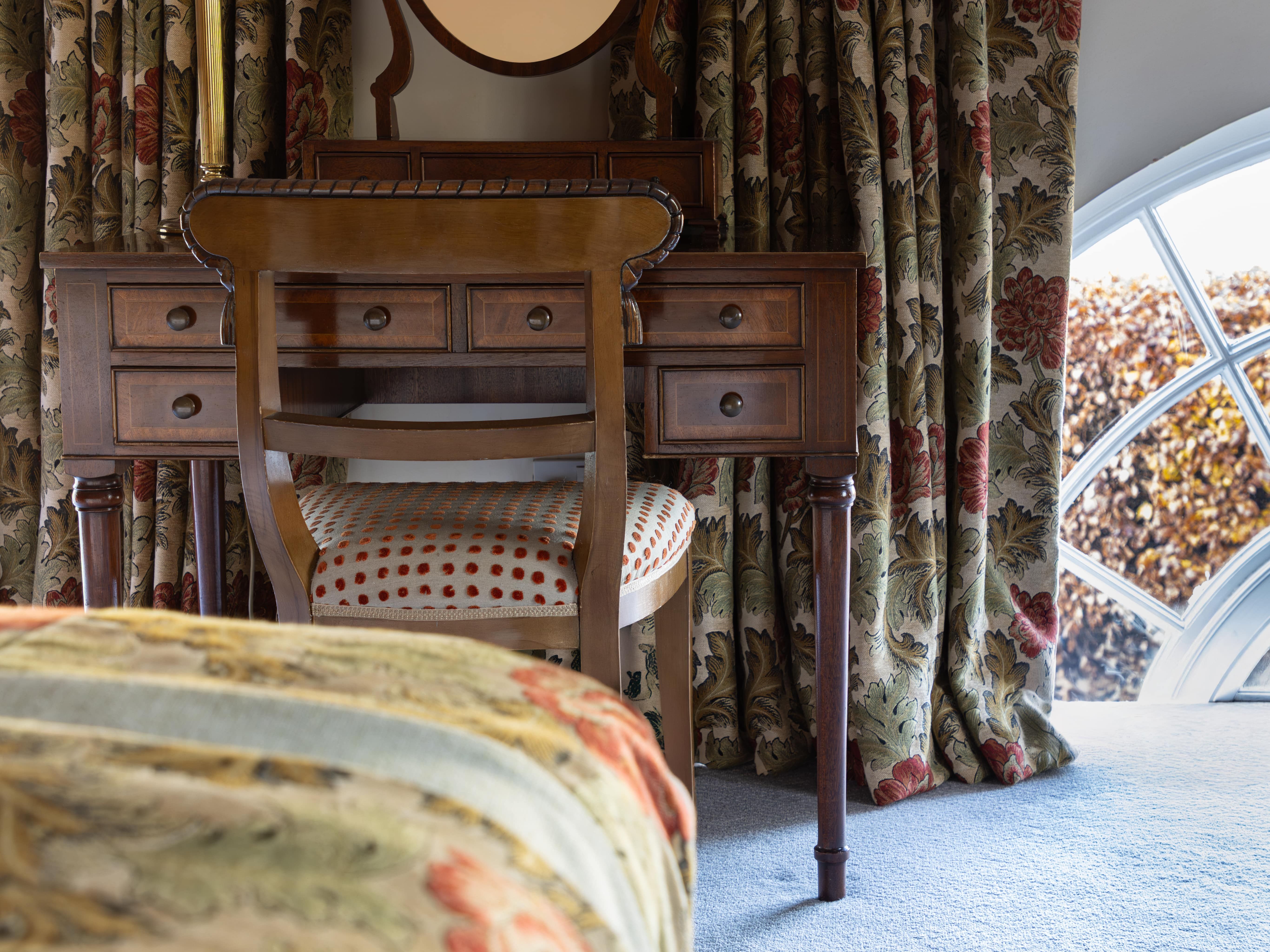 Traditional bedroom with floral curtains, wooden vanity, chair, and lamp