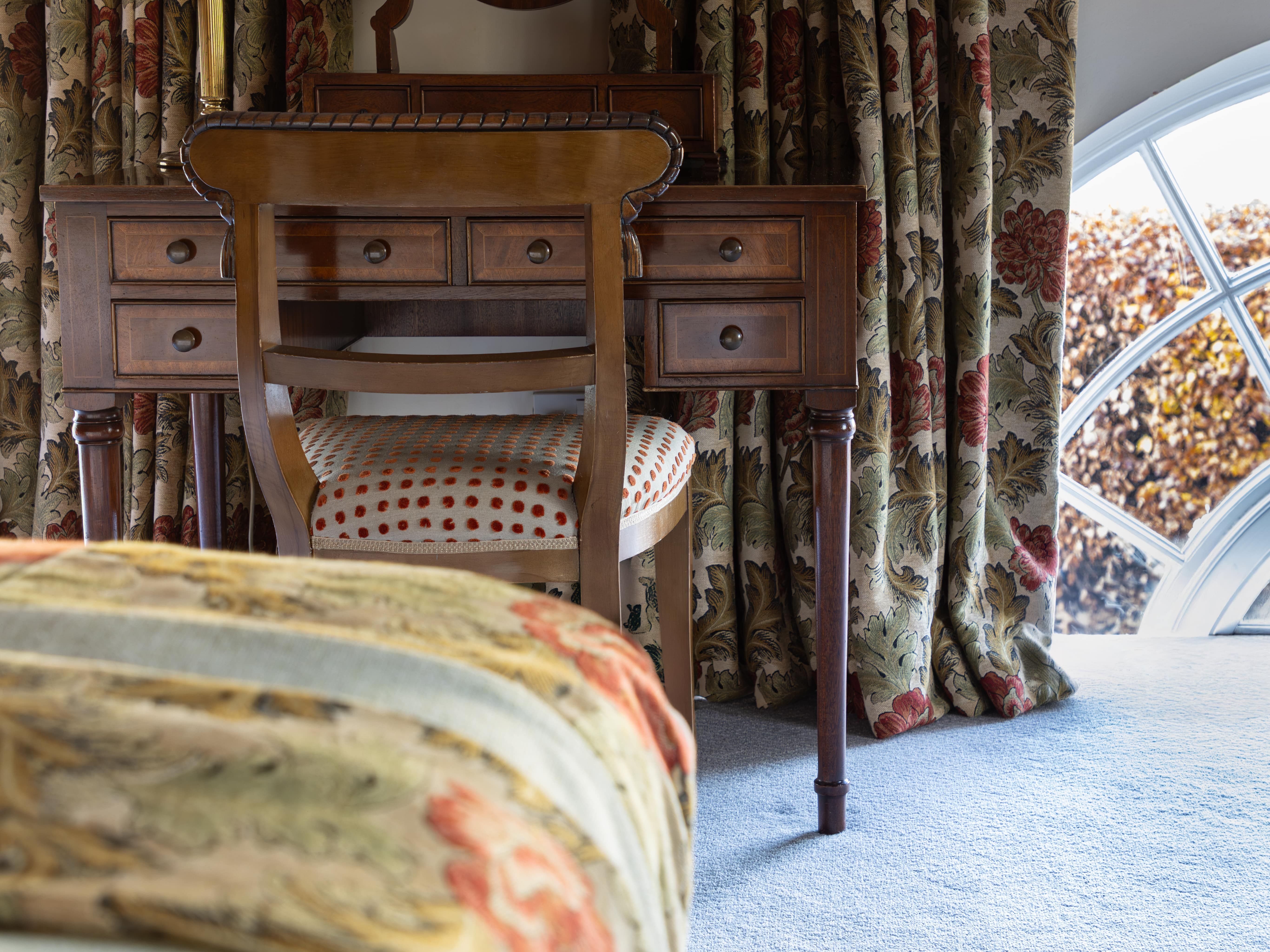 Traditional bedroom with floral curtains, wooden vanity, chair, and lamp