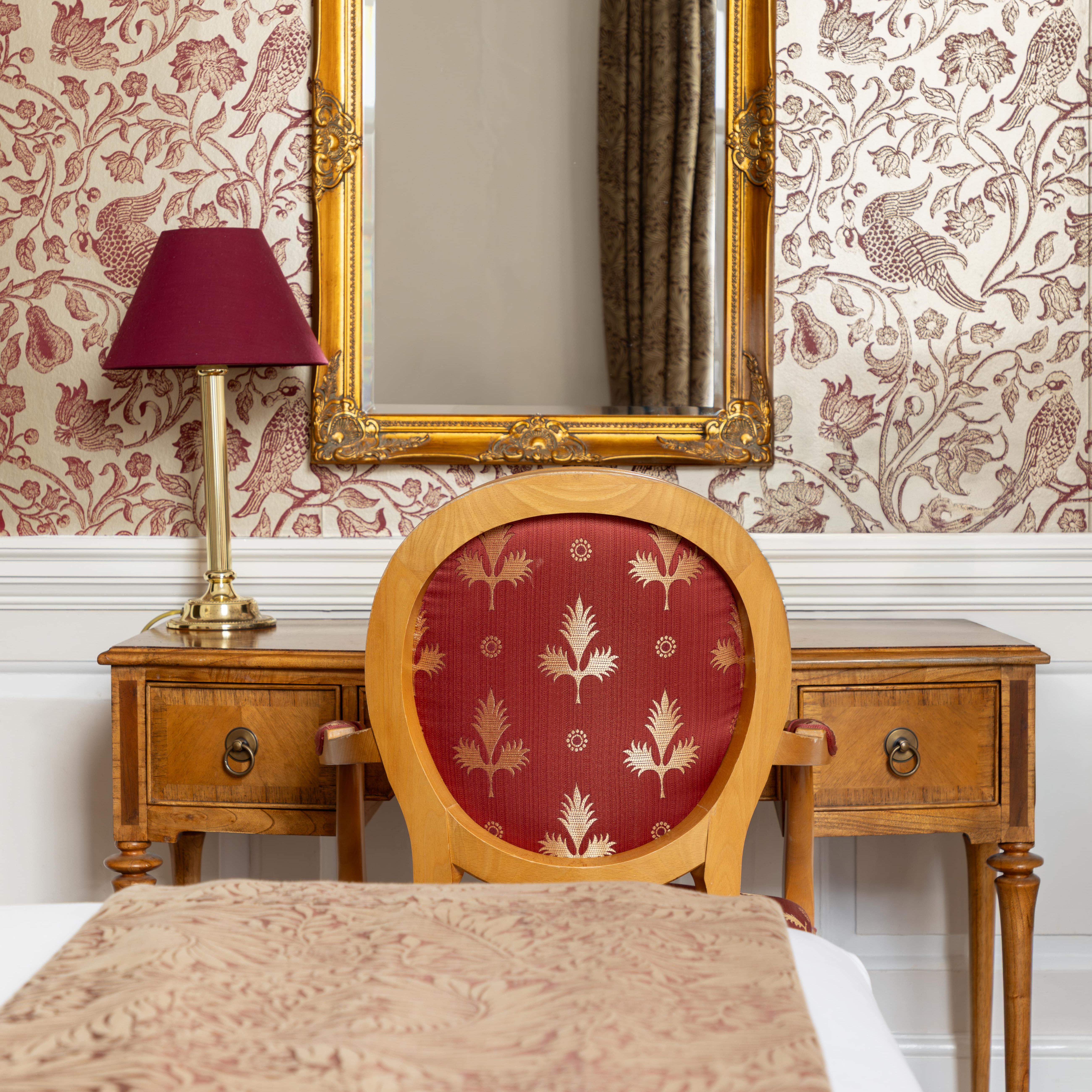 Elegant bedroom with a vintage wooden desk, ornate gold-framed mirror, and red-patterned chair