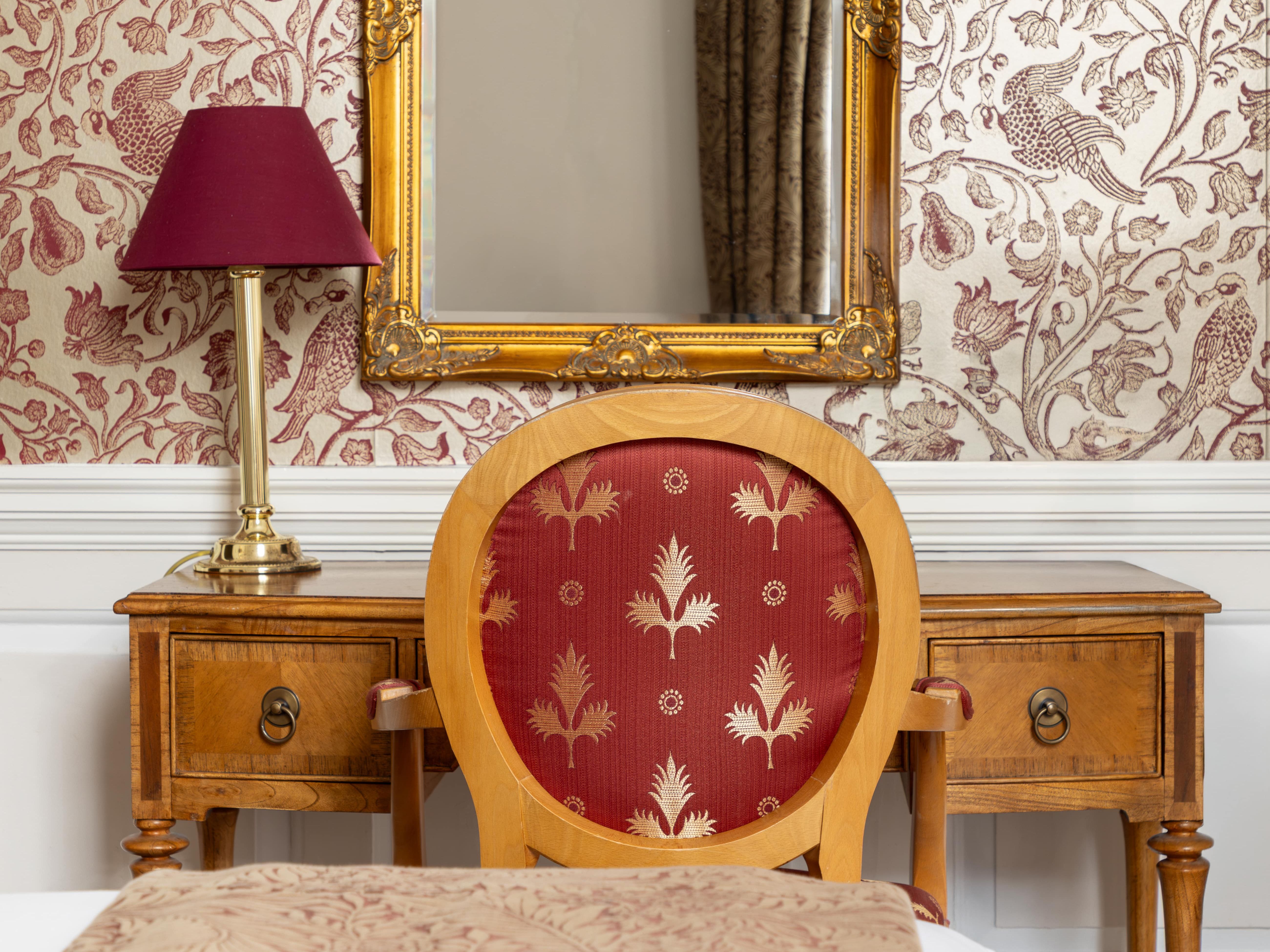 Elegant bedroom with a vintage wooden desk, ornate gold-framed mirror, and red-patterned chair