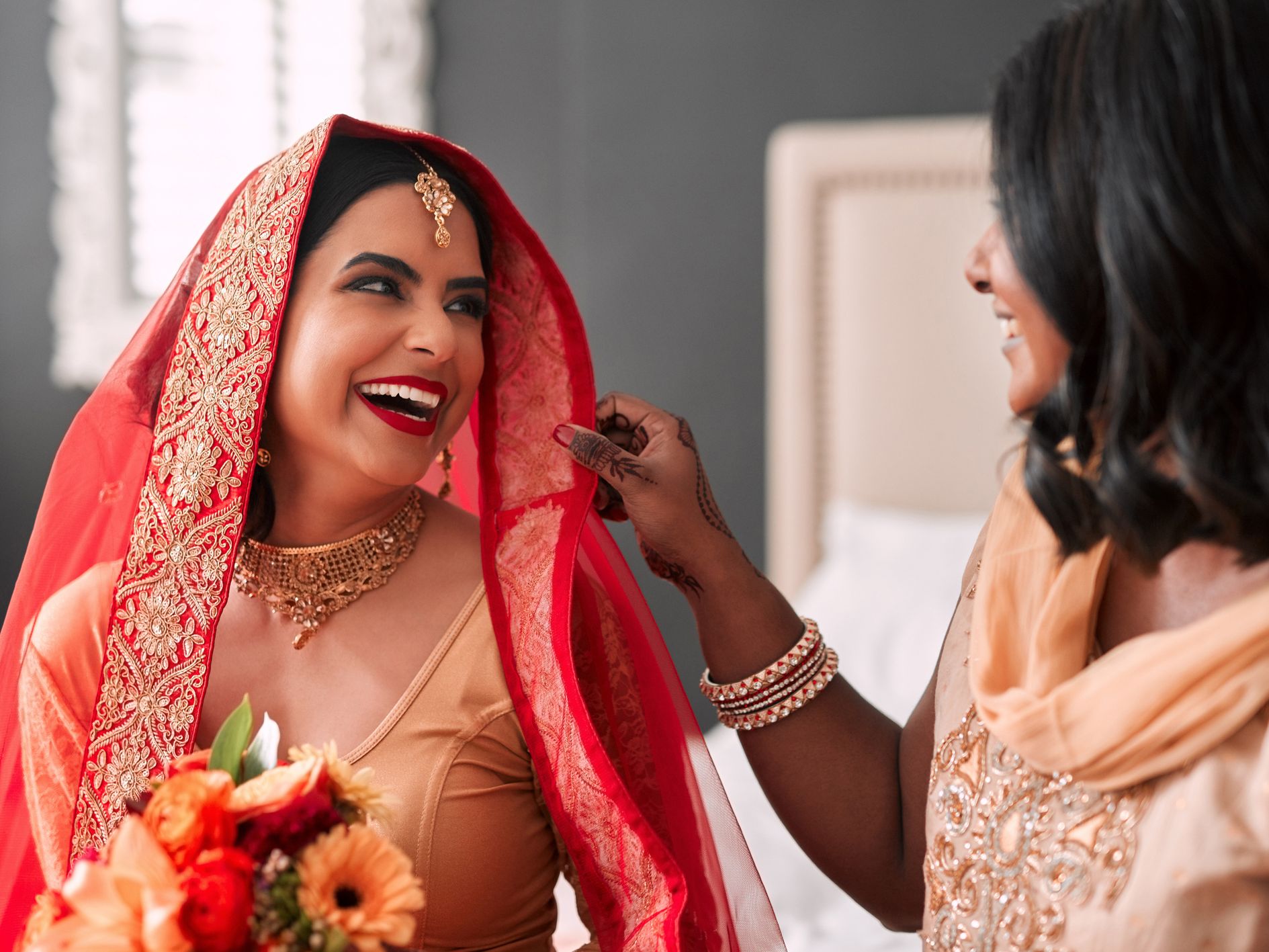 Smiling bride in traditional attire with another woman adjusting her veil