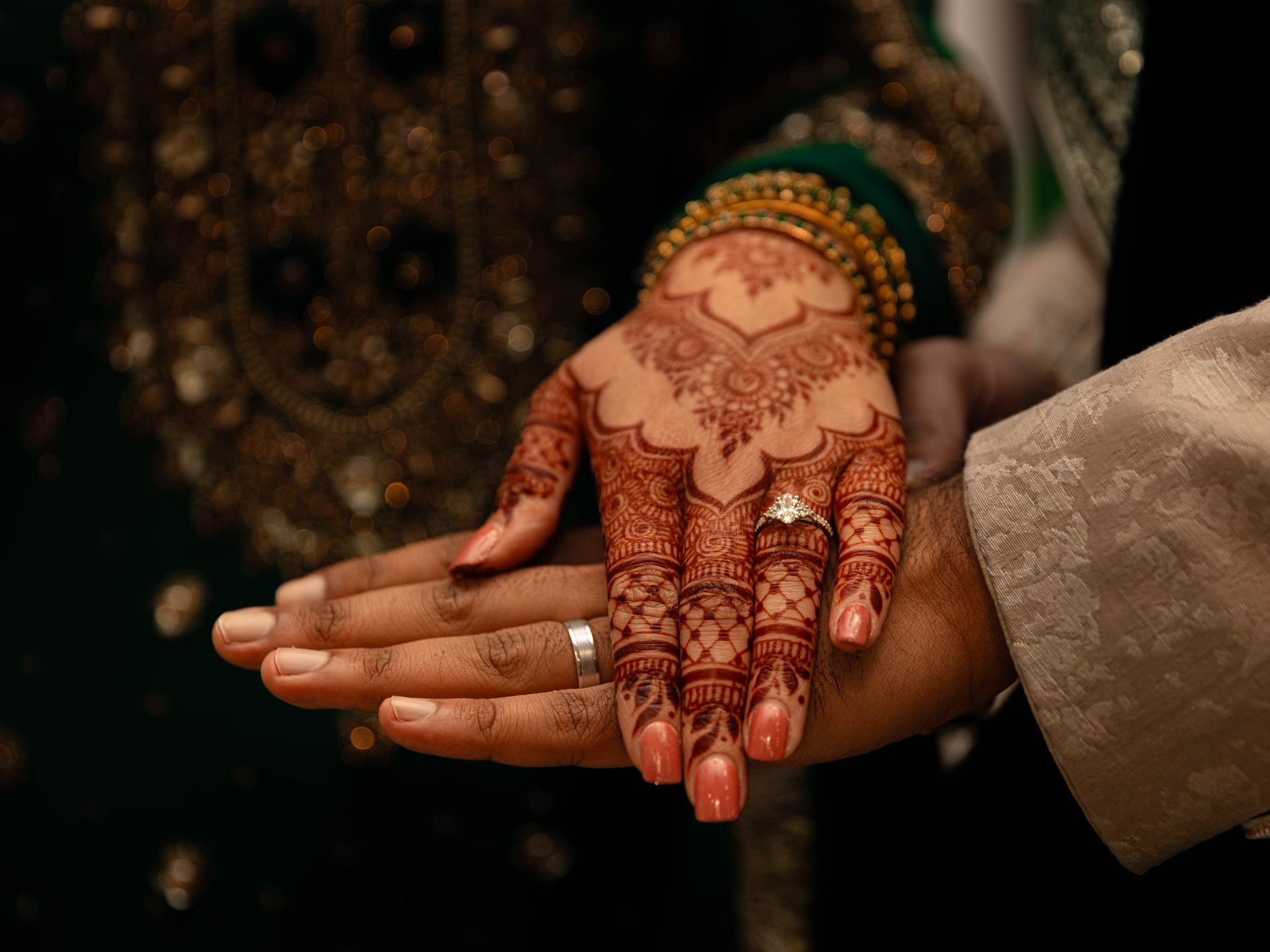 Close-up of a bride and groom's hands with intricate henna designs and wedding rings