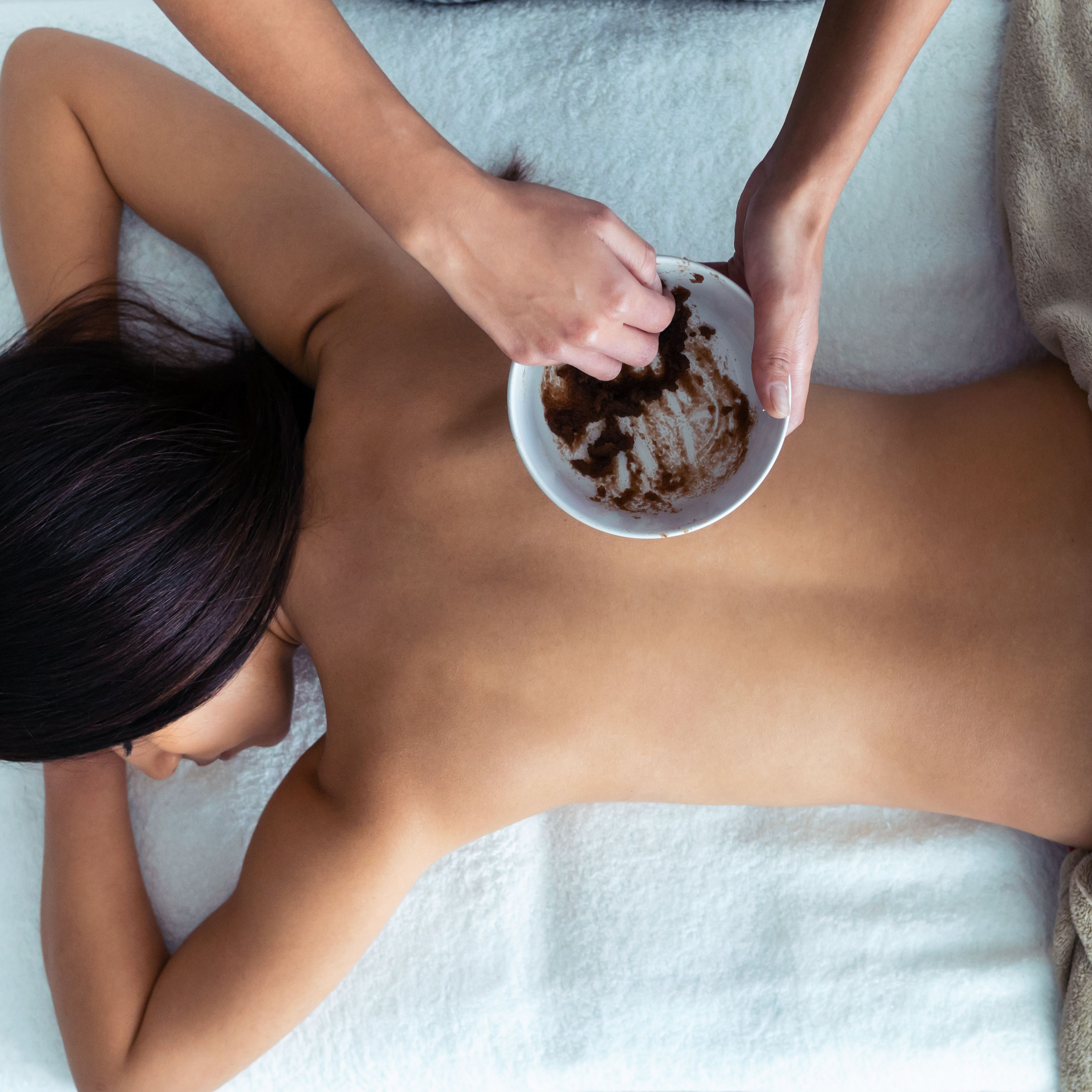 Person receiving a back massage with a scrub mixture in a spa setting