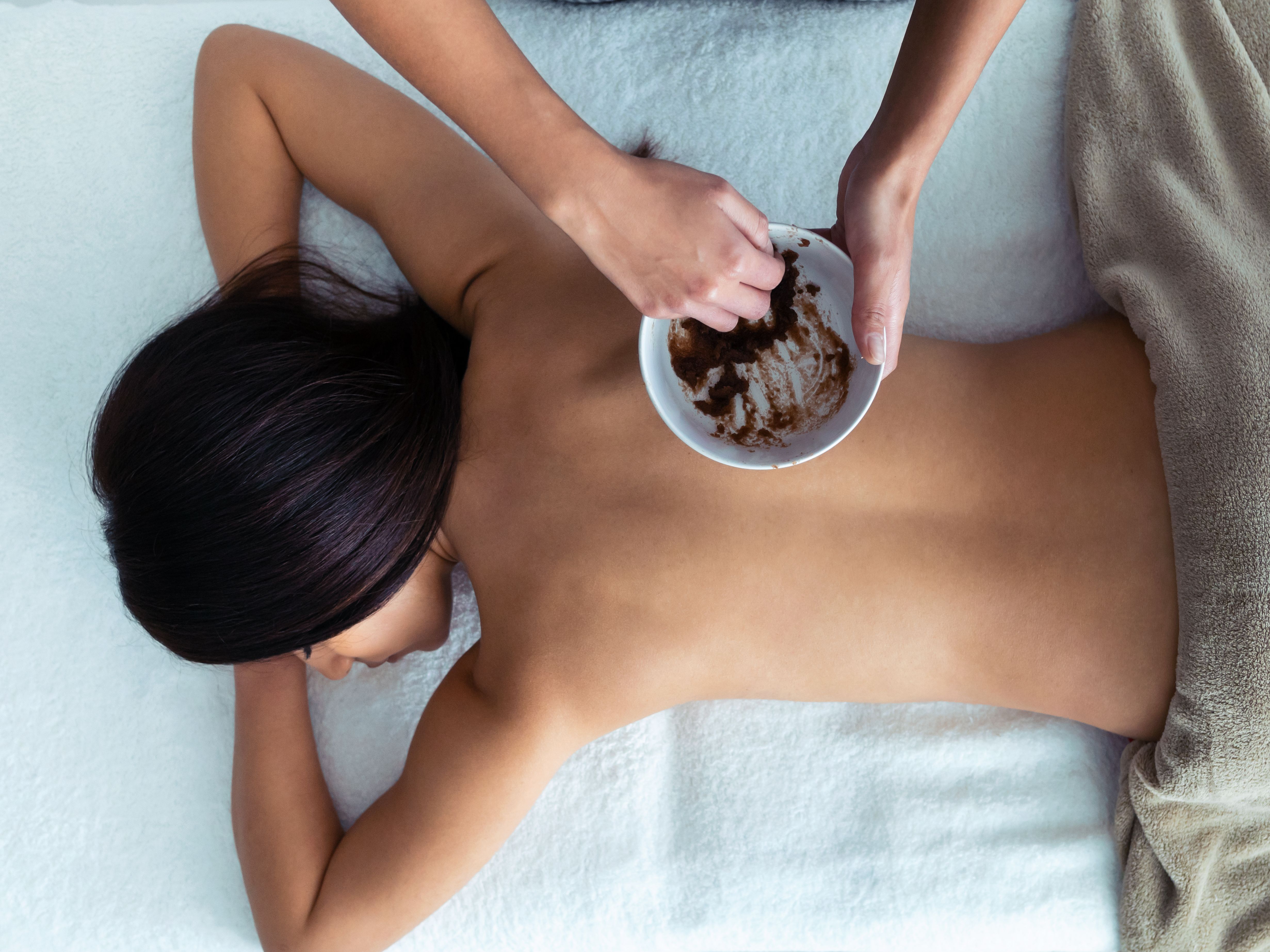 Person receiving a back massage with a scrub mixture in a spa setting