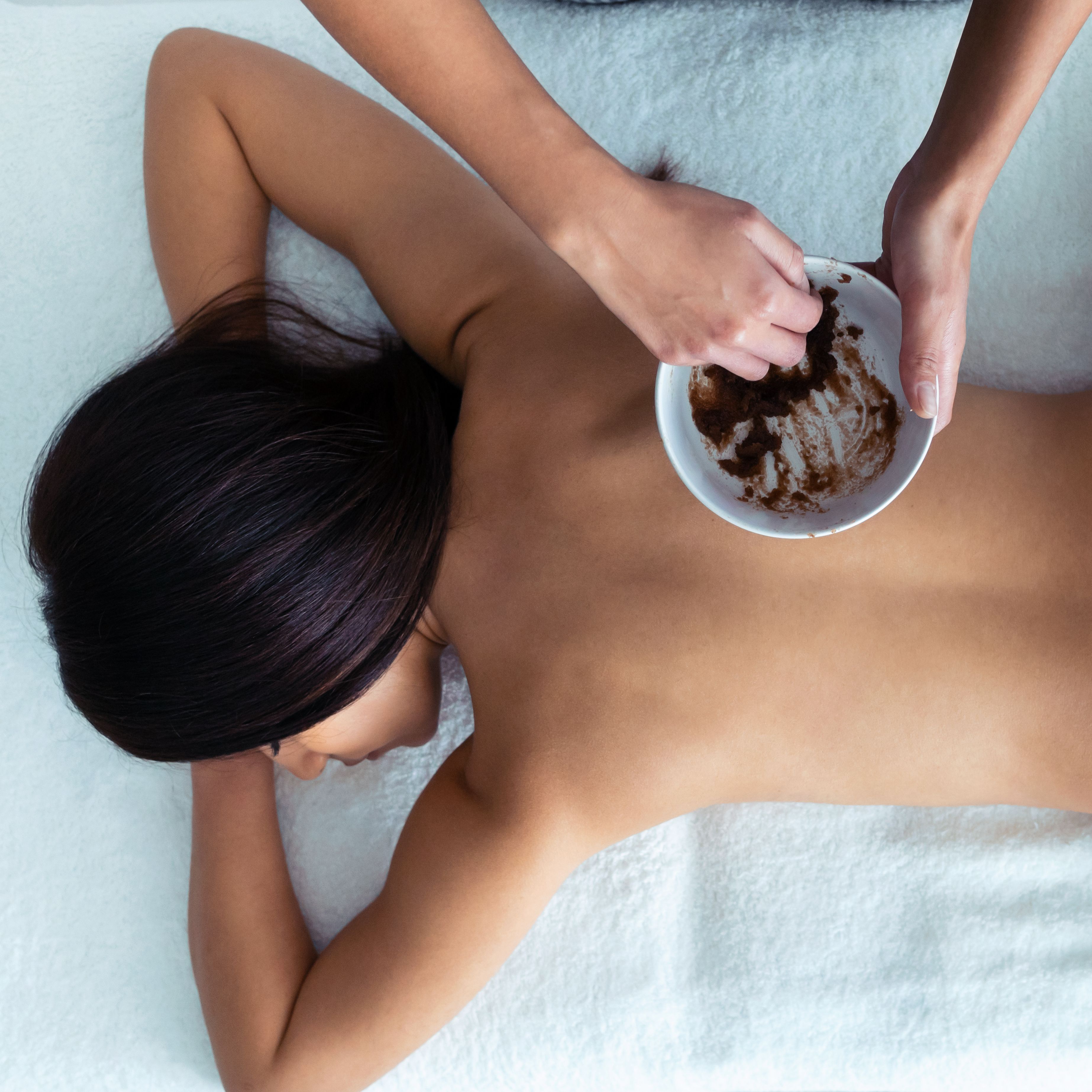 Person receiving a back massage with a scrub mixture in a spa setting