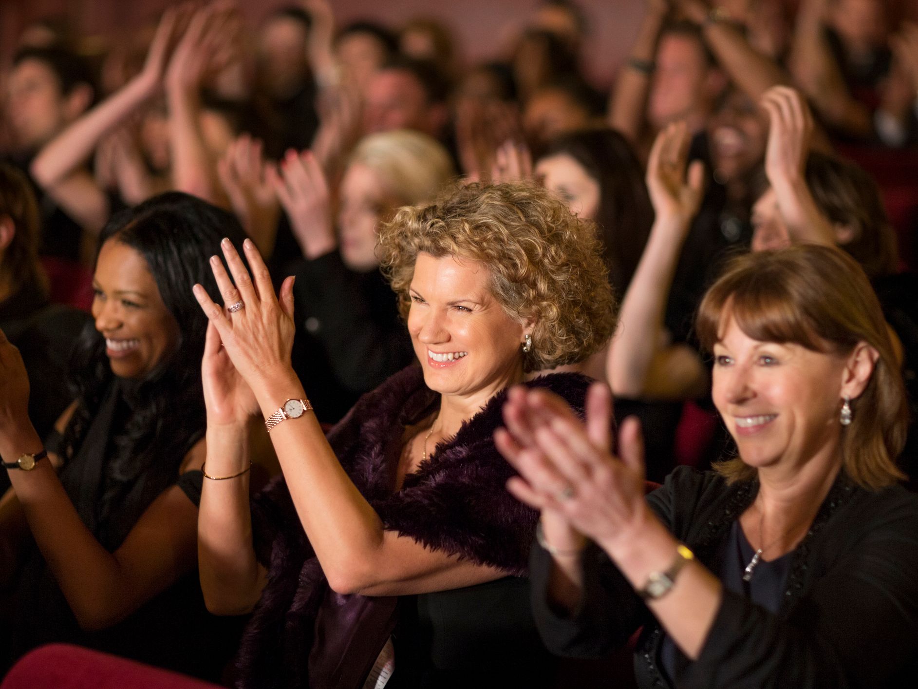 Audience members smiling and clapping enthusiastically at an event.
