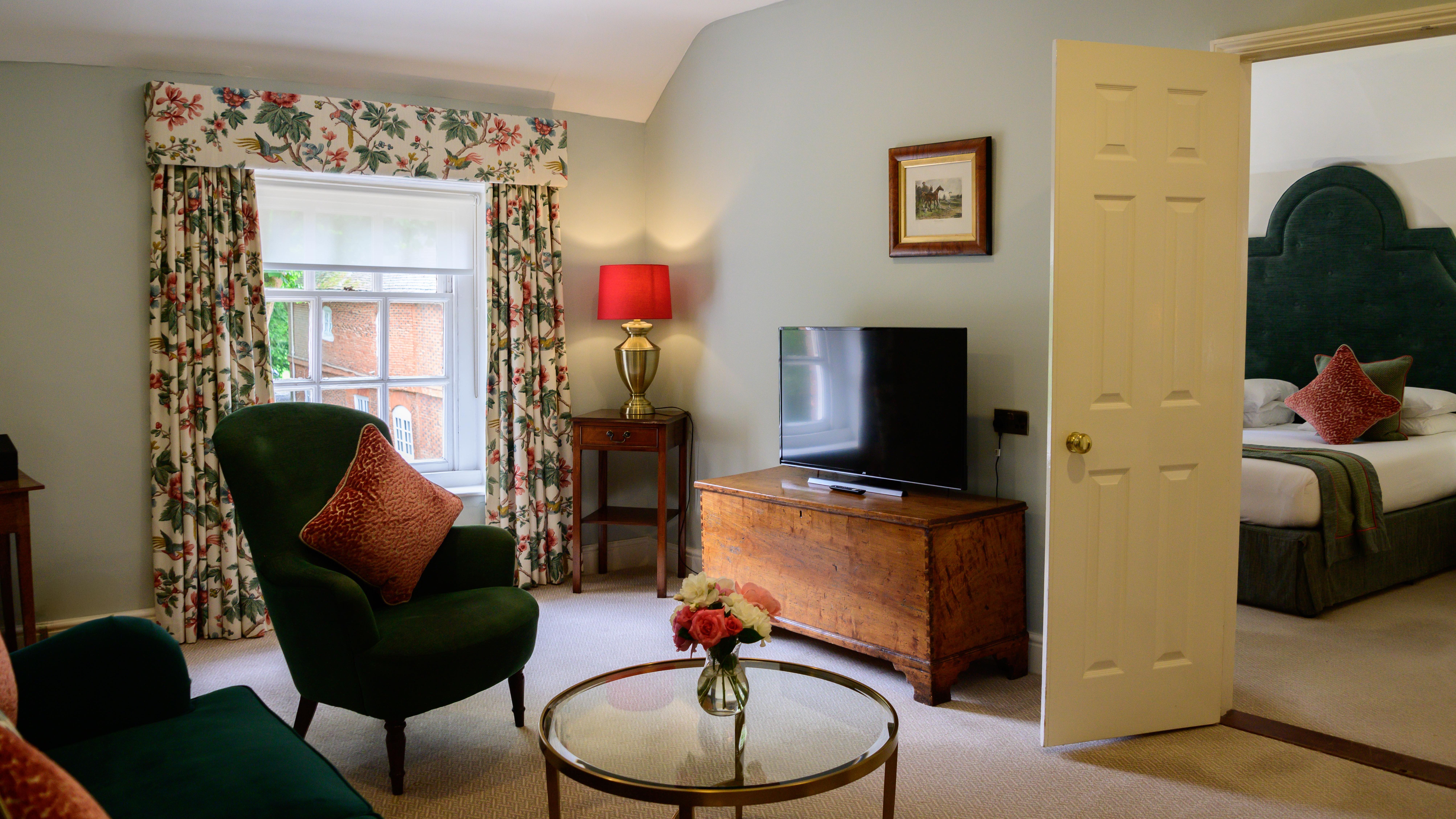 Cozy living room with armchair, floral curtains, and view into bedroom