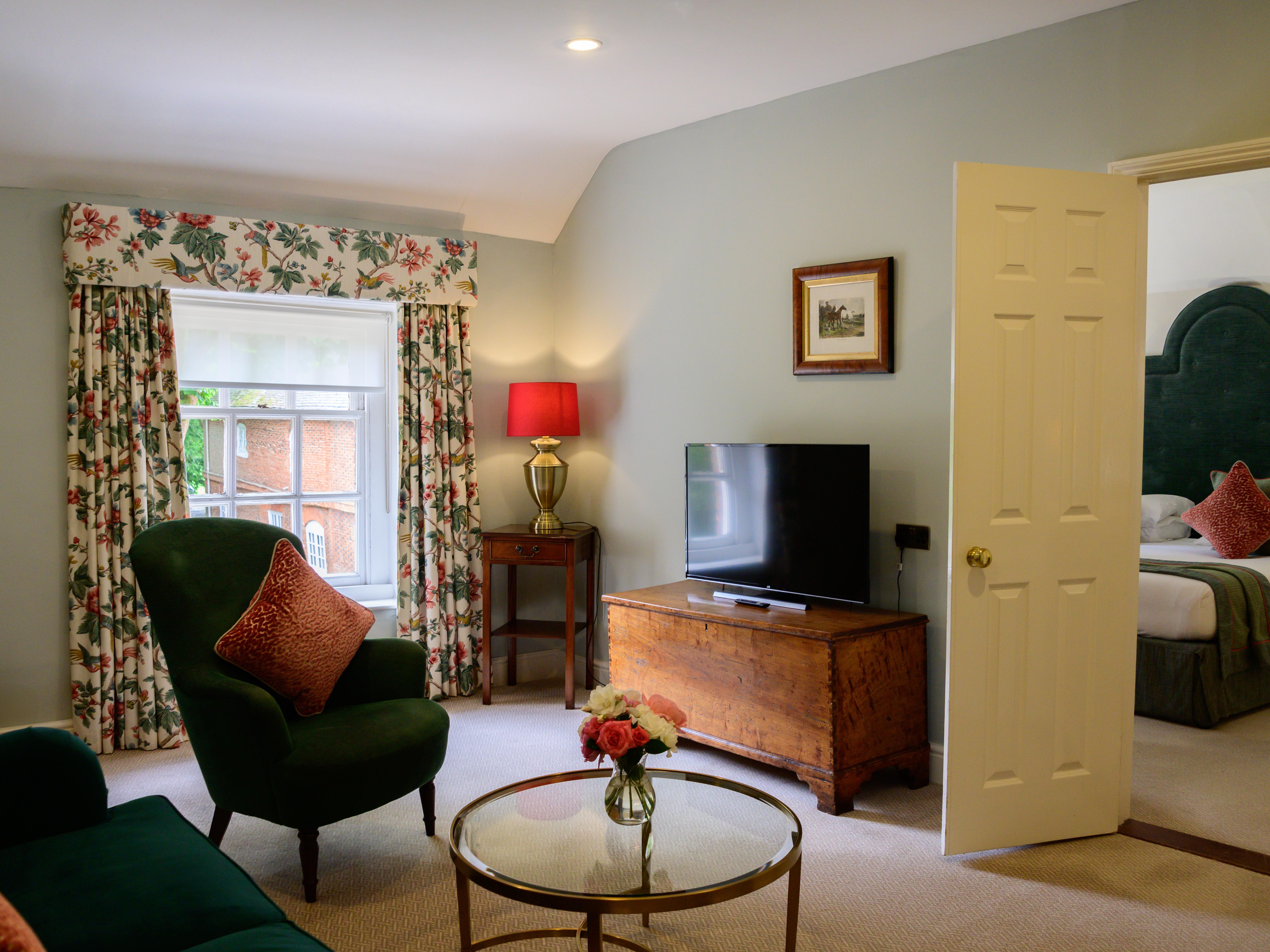 Cozy living room with armchair, floral curtains, and view into bedroom