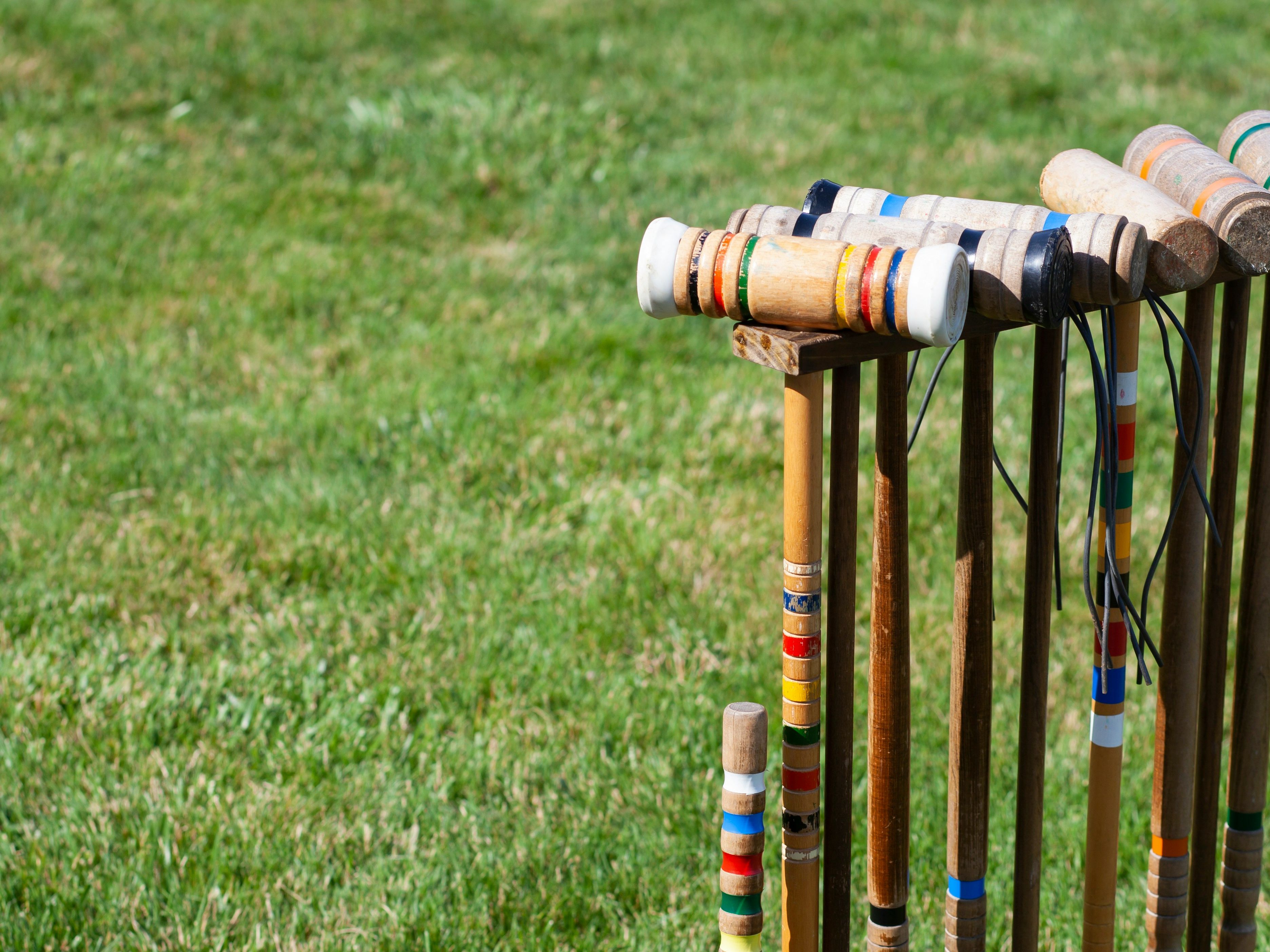 Croquet mallets and balls arranged in a wooden stand on a grassy lawn.