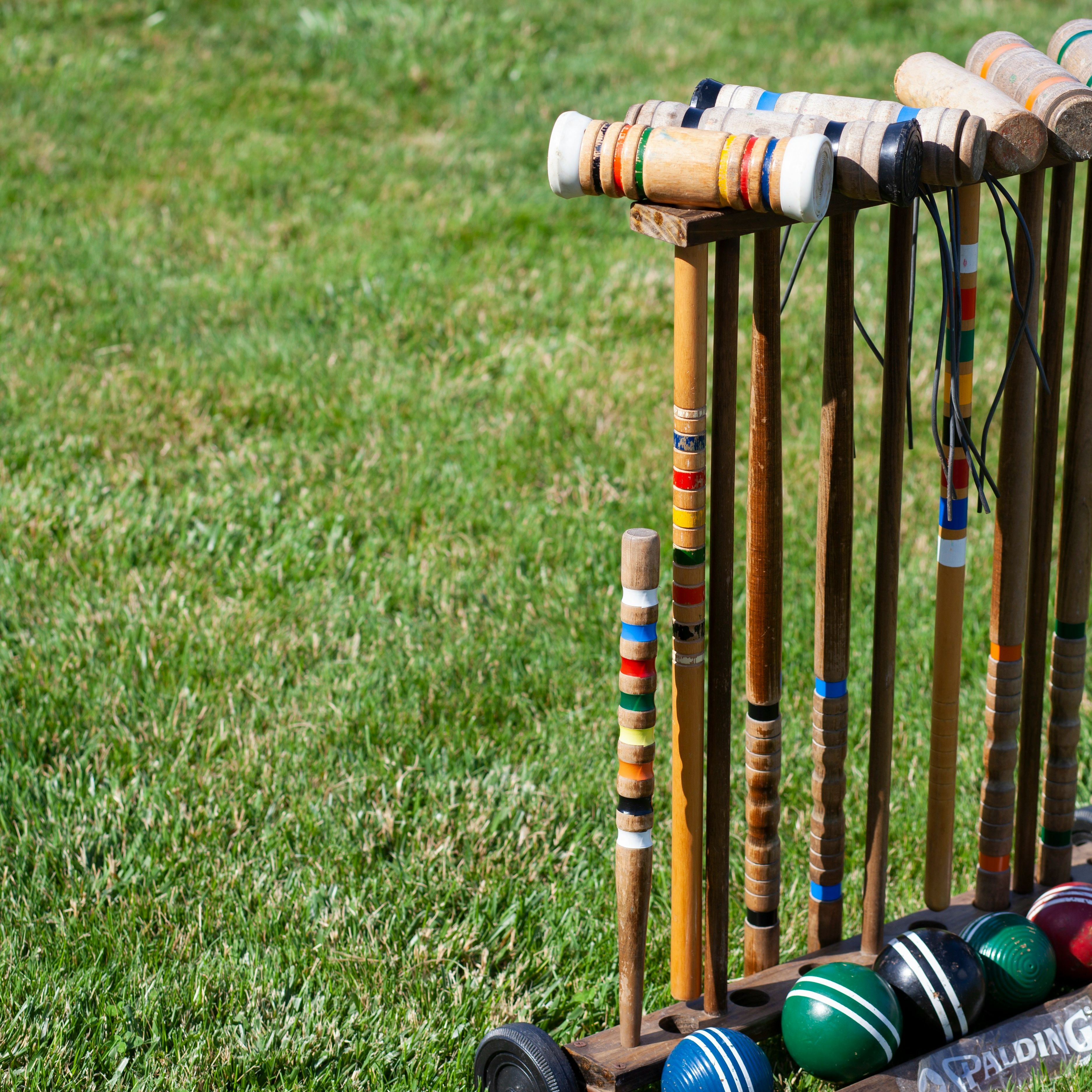 Croquet mallets and balls arranged in a wooden stand on a grassy lawn.