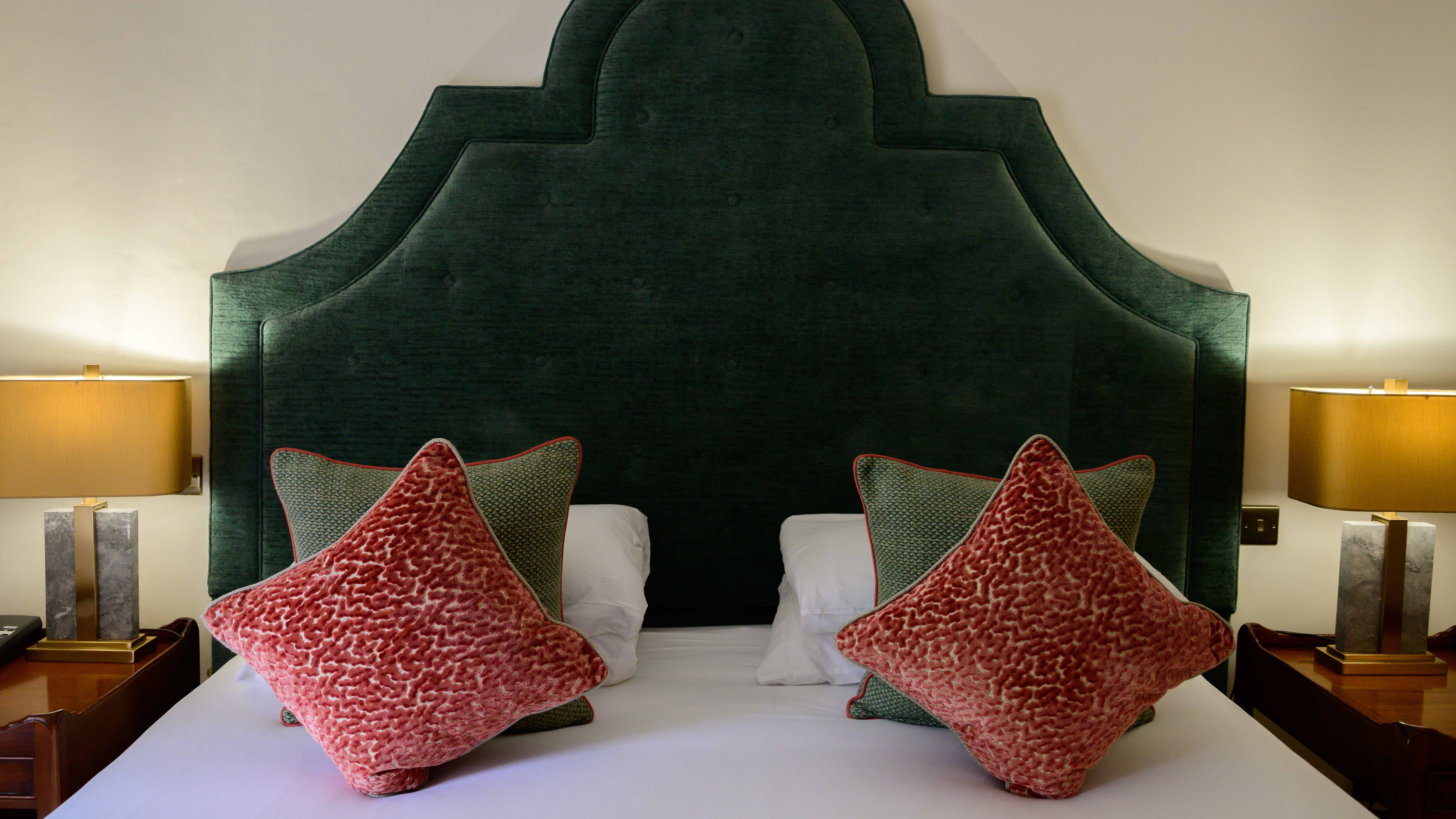 Bed with large upholstered headboard, two bedside lamps, and decorative pillows