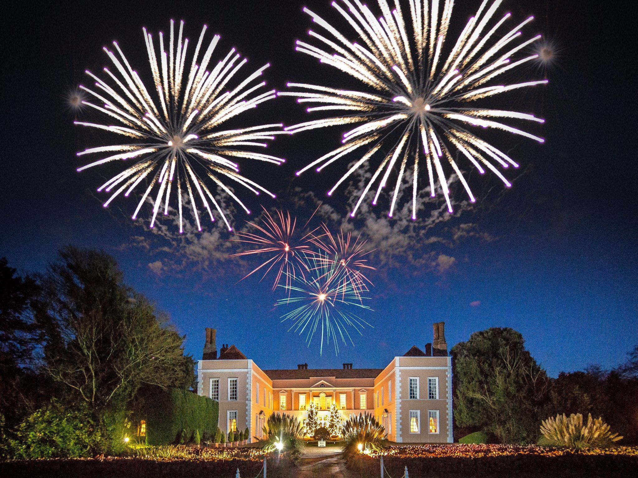 Large manor house illuminated at night with colorful fireworks lighting up the sky above.