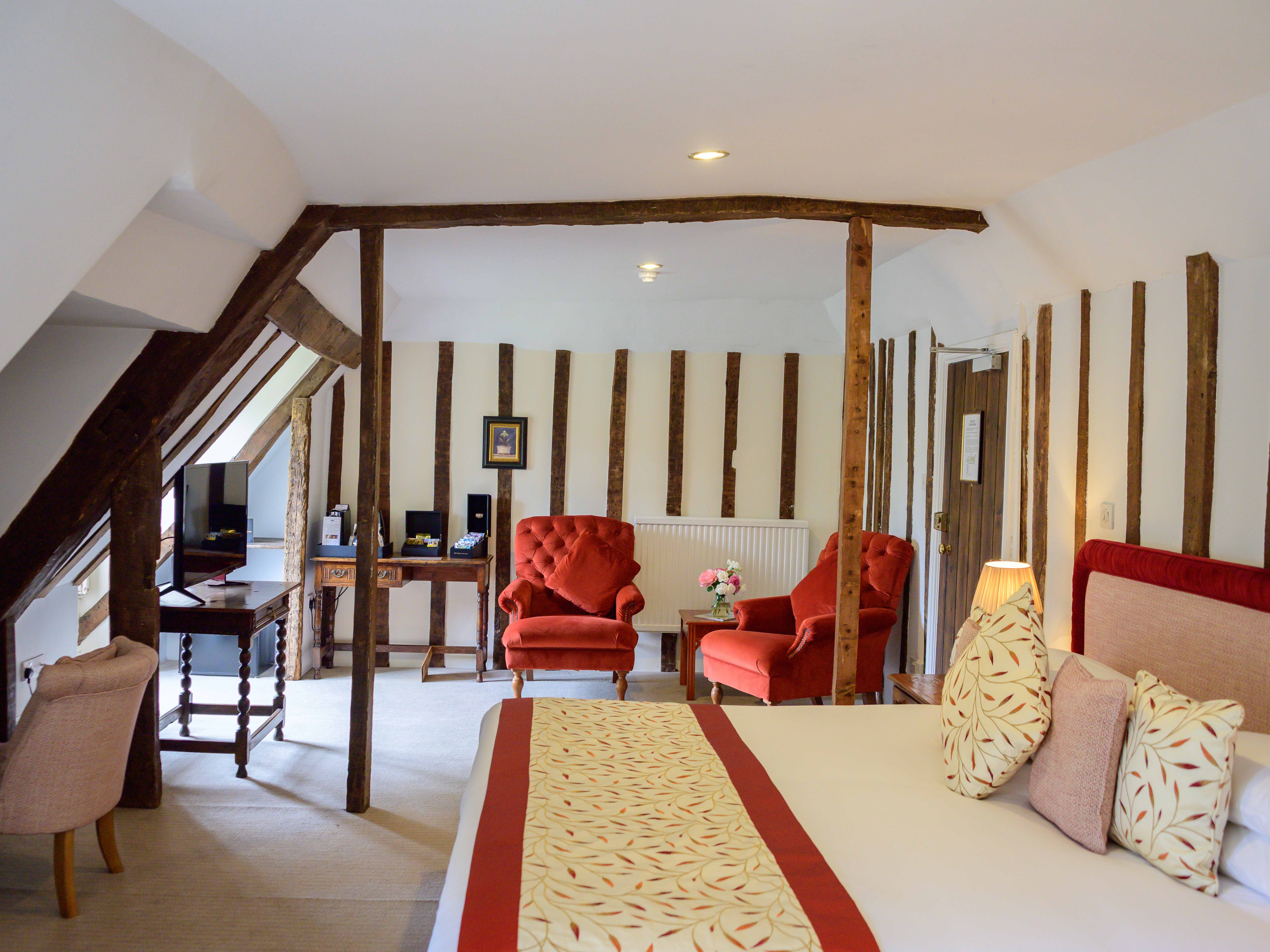 Cozy hotel room with exposed wooden beams, red armchairs, and a comfortable bed