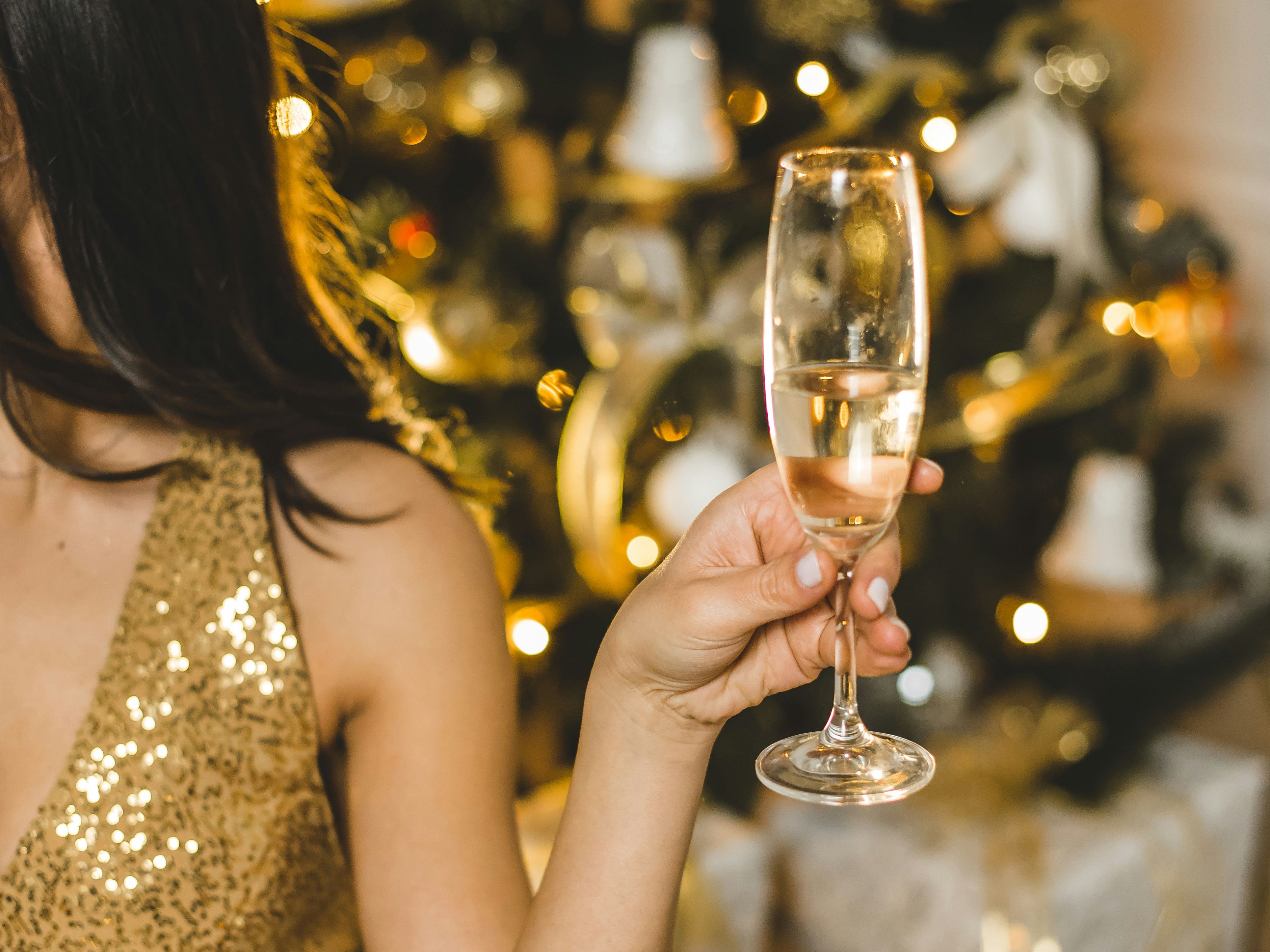 Woman in a sparkling gold dress holding a champagne glass in front of a decorated Christmas tree
