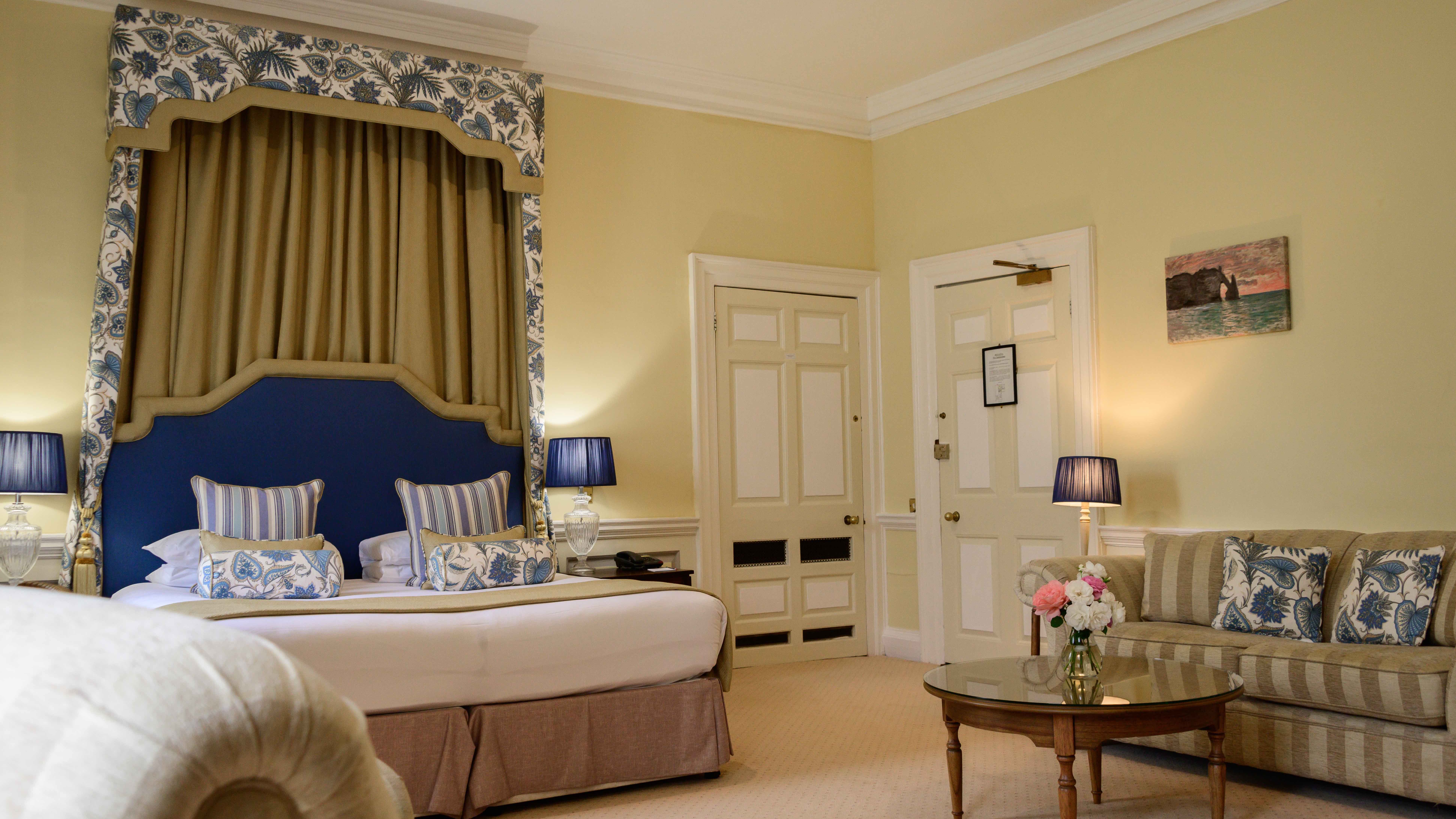 Elegant hotel room with a large bed, sofa, glass coffee table, and classic decor