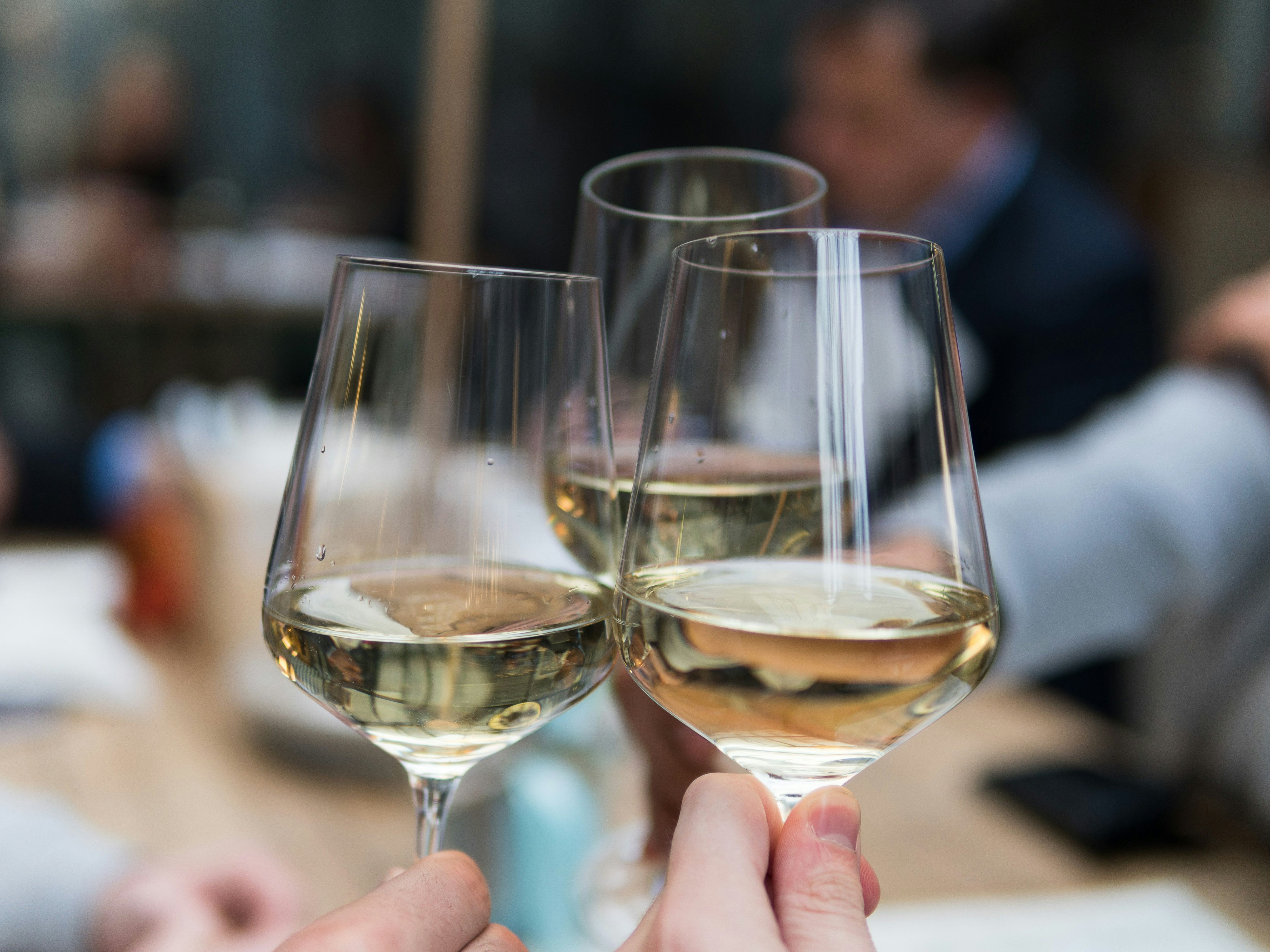 Three people clinking glasses of white wine at a gathering