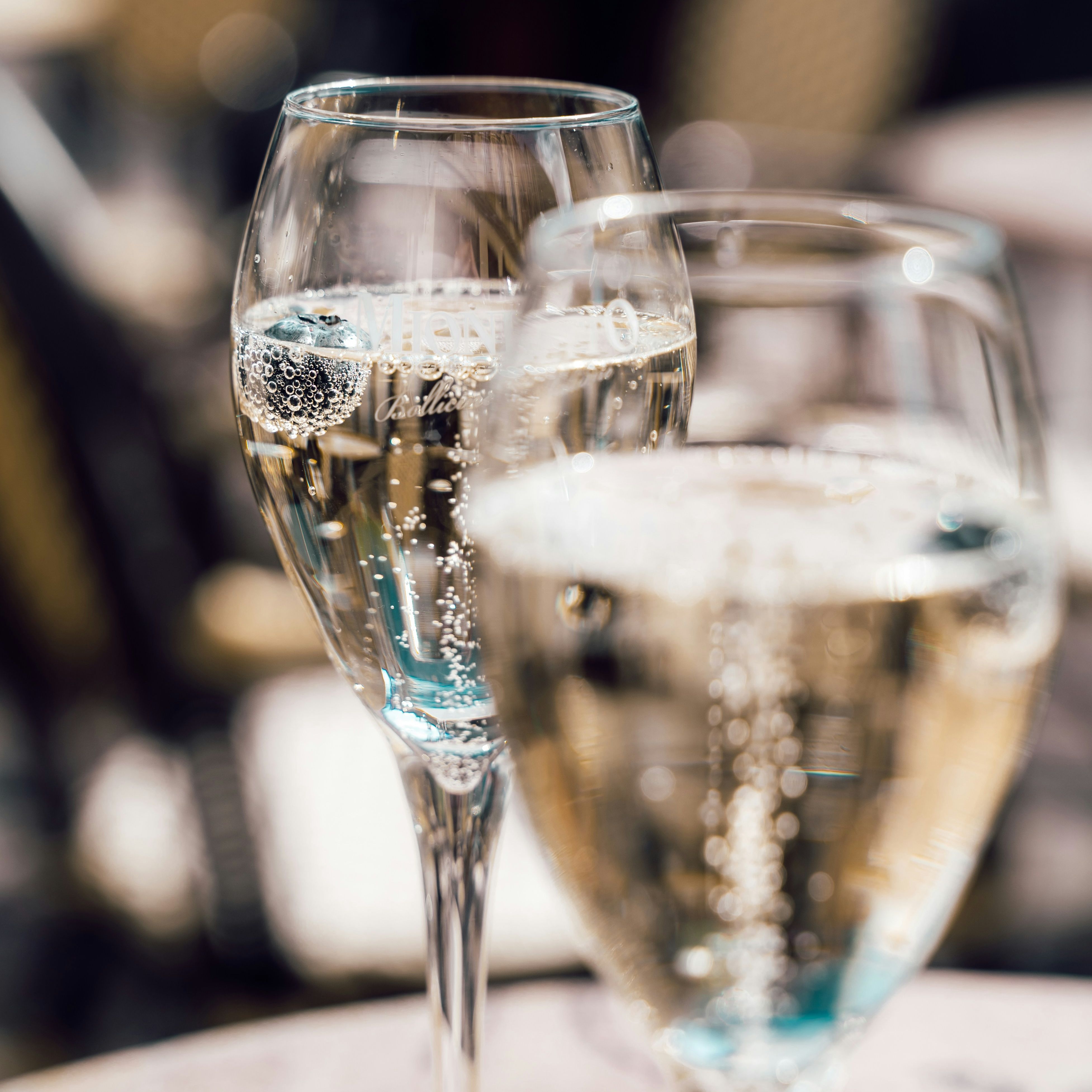 Two glasses of sparkling wine with bubbles, set on an outdoor table.