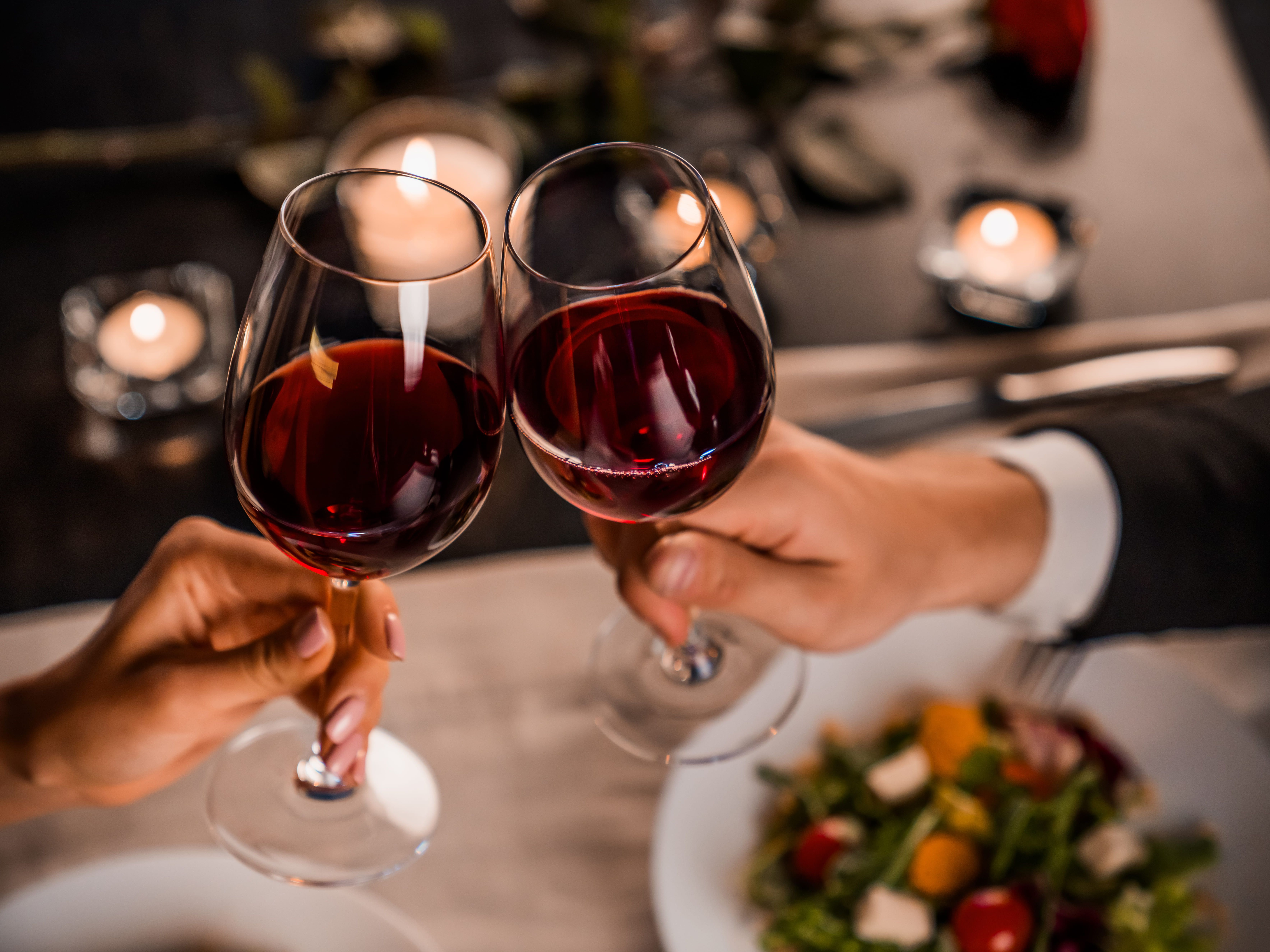 Couple clinking glasses of red wine over a romantic dinner table with candles.