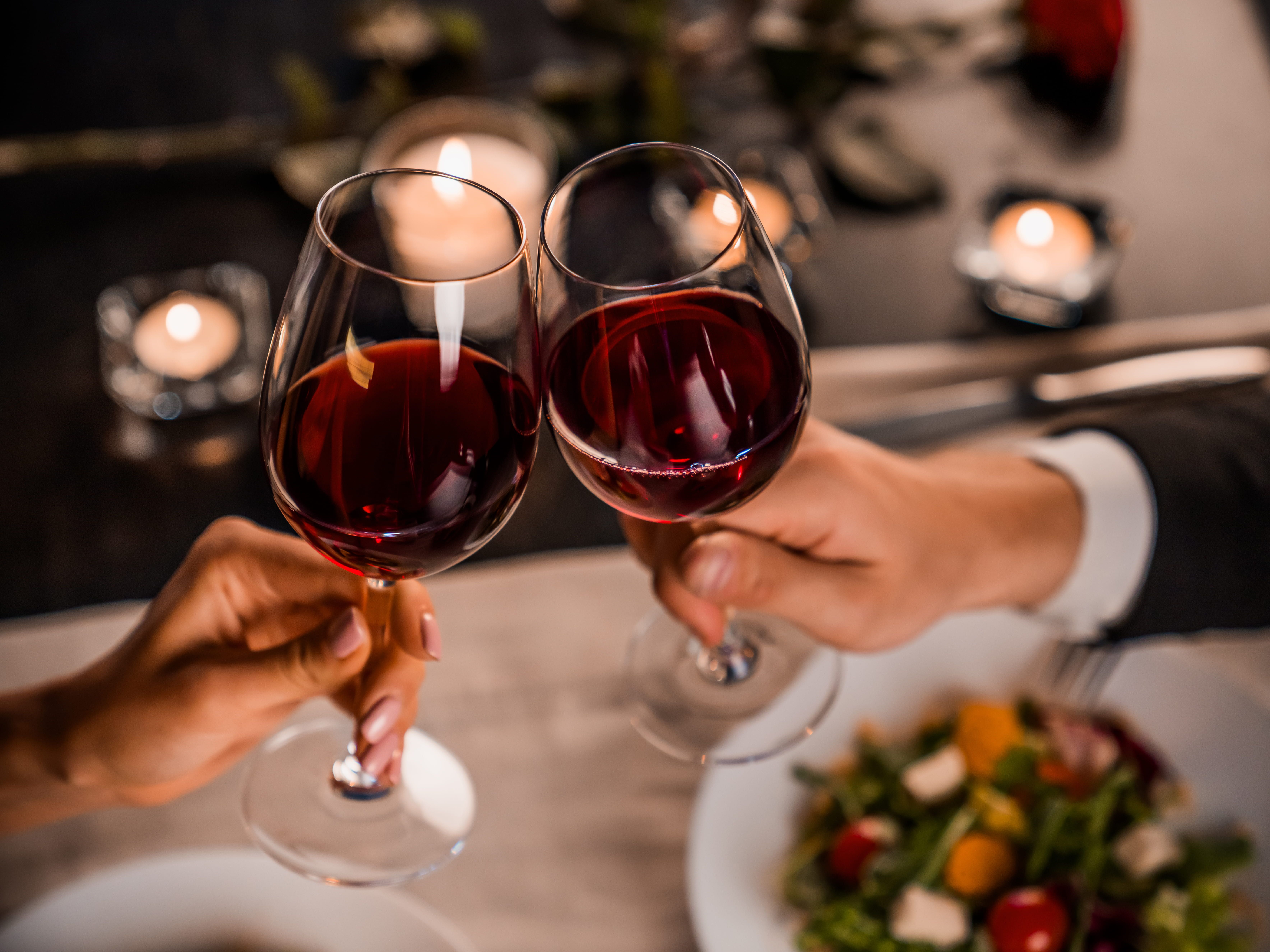 Couple clinking glasses of red wine over a romantic dinner table with candles.