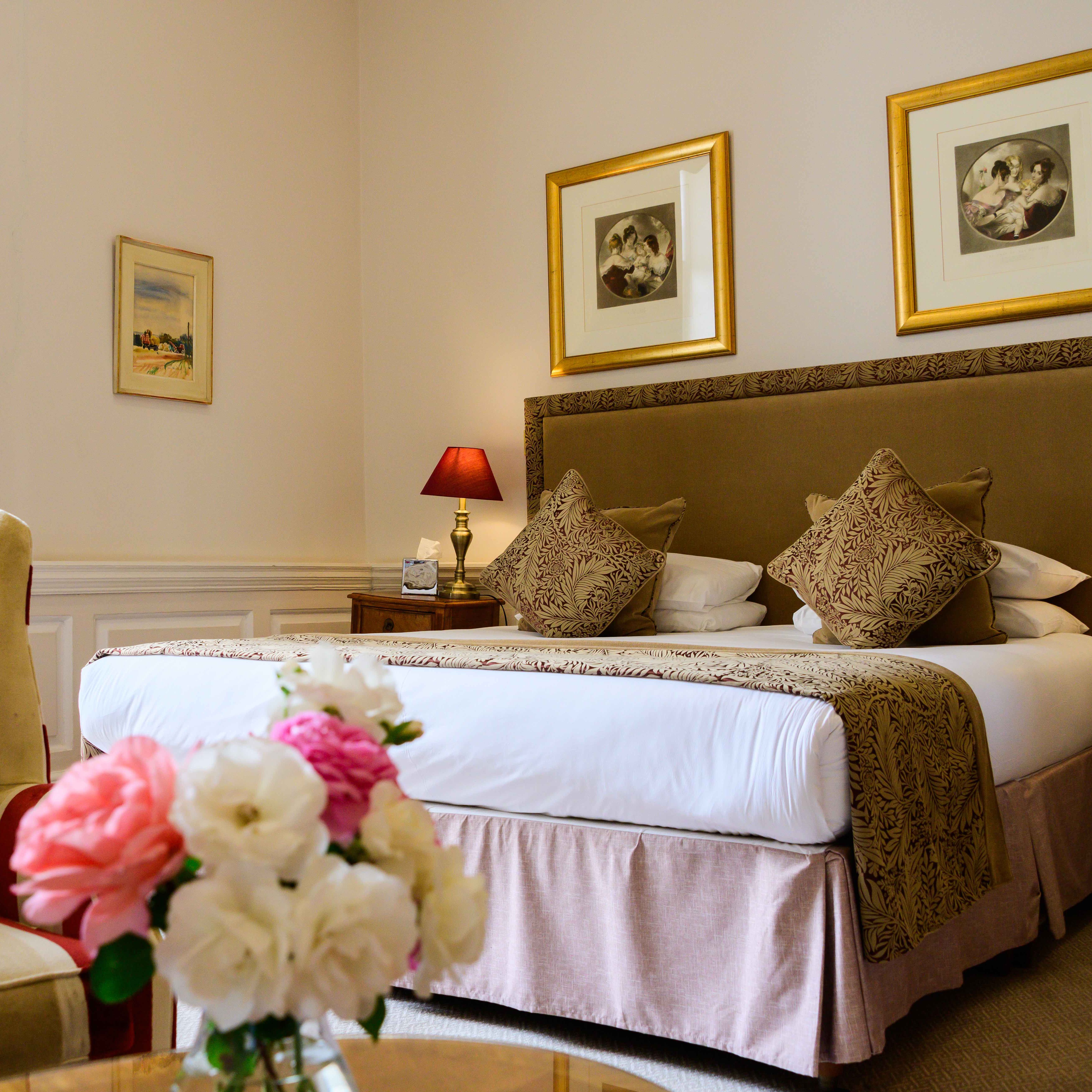 Elegant hotel room with large bed, armchair, and flowers on a table