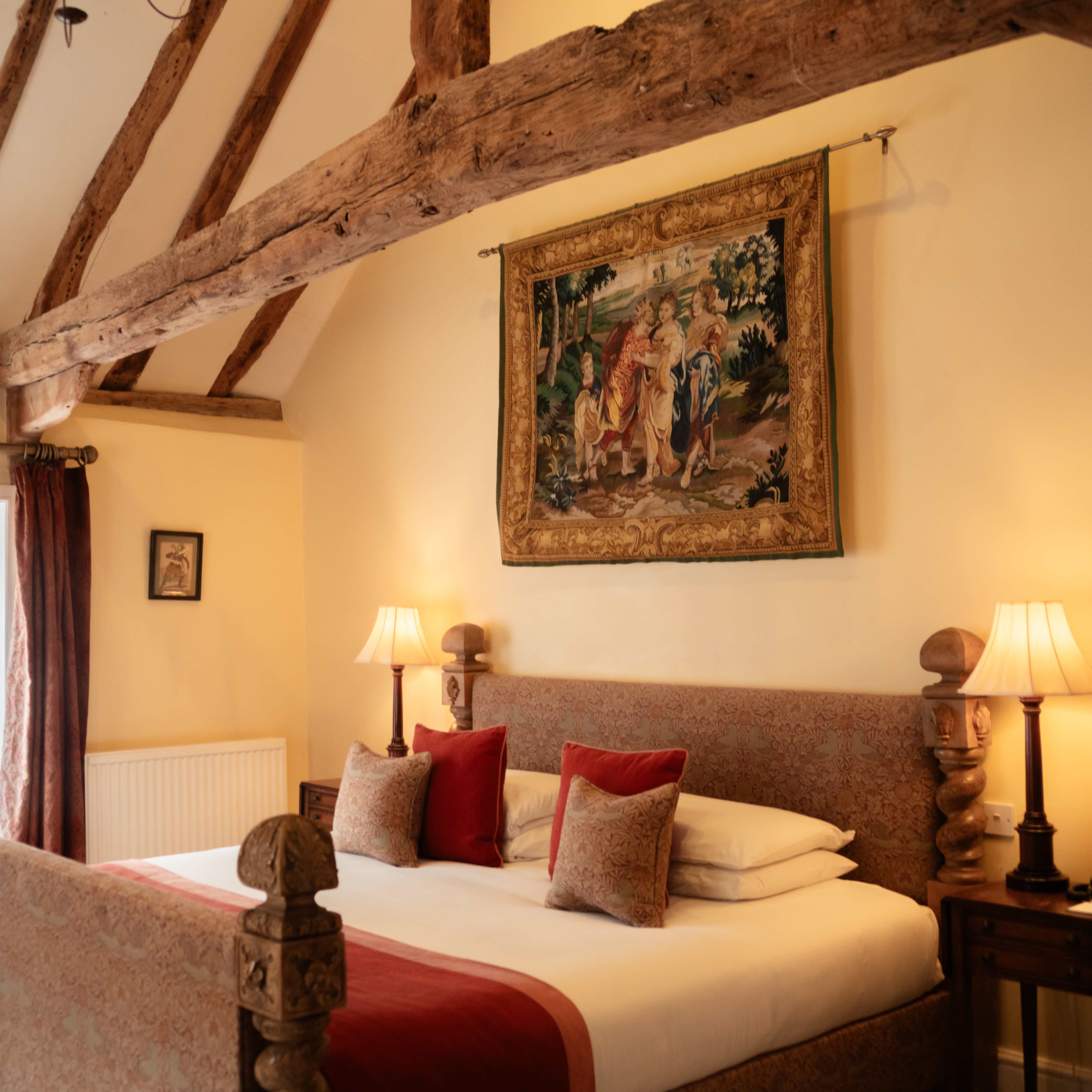 Elegant hotel bedroom with exposed wooden beams, tapestry, and warm lighting.