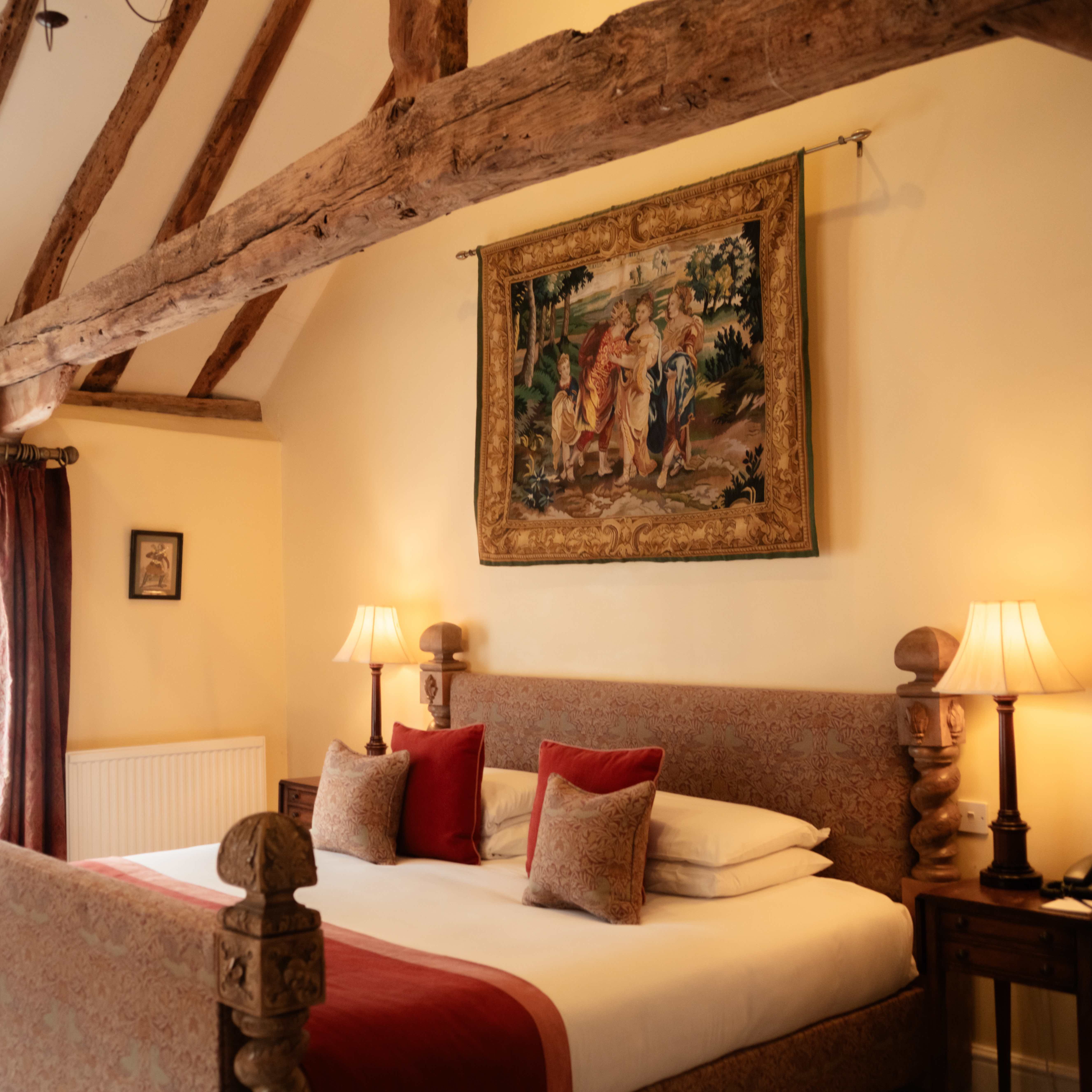 Elegant hotel bedroom with exposed wooden beams, tapestry, and warm lighting.