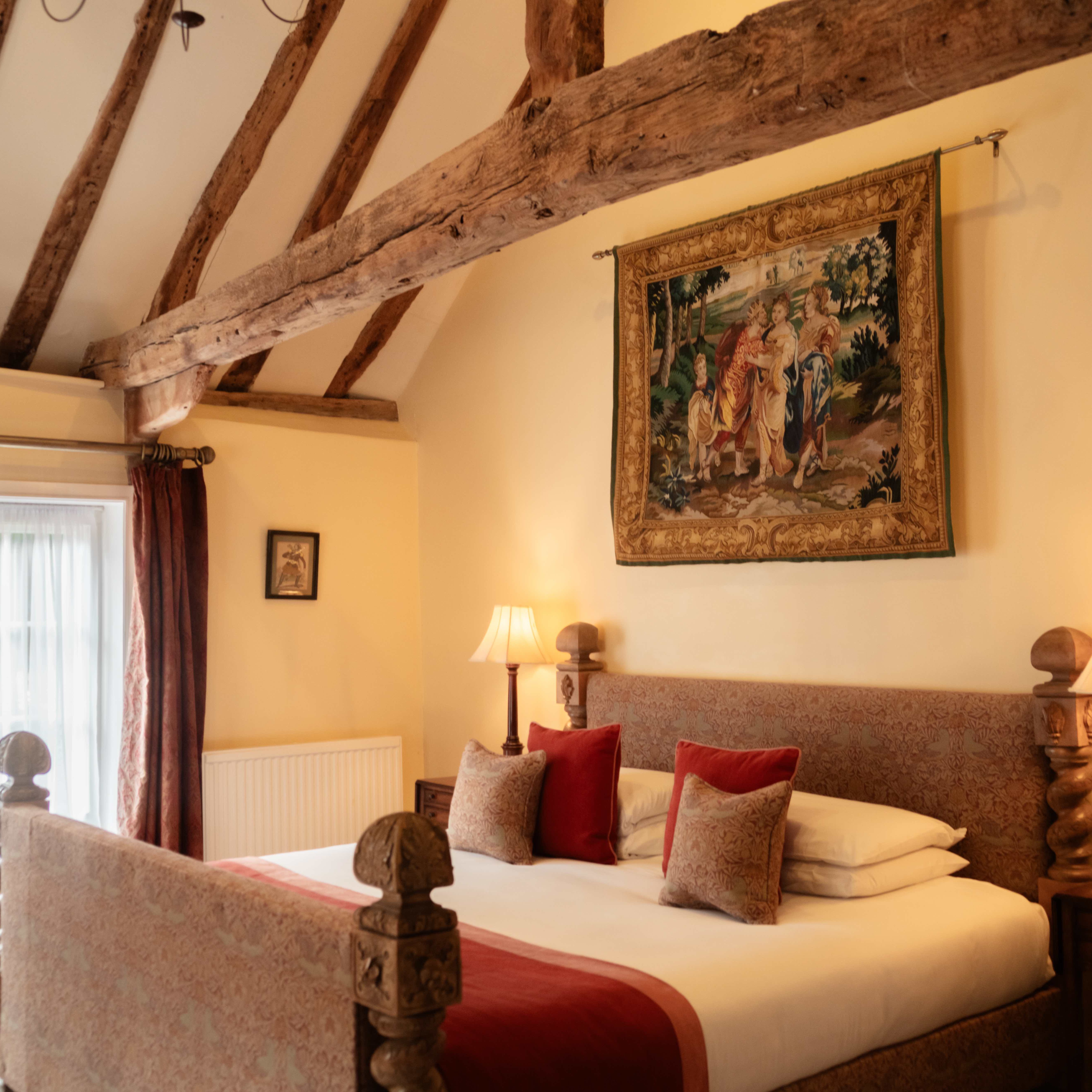 Elegant hotel bedroom with exposed wooden beams, tapestry, and warm lighting.