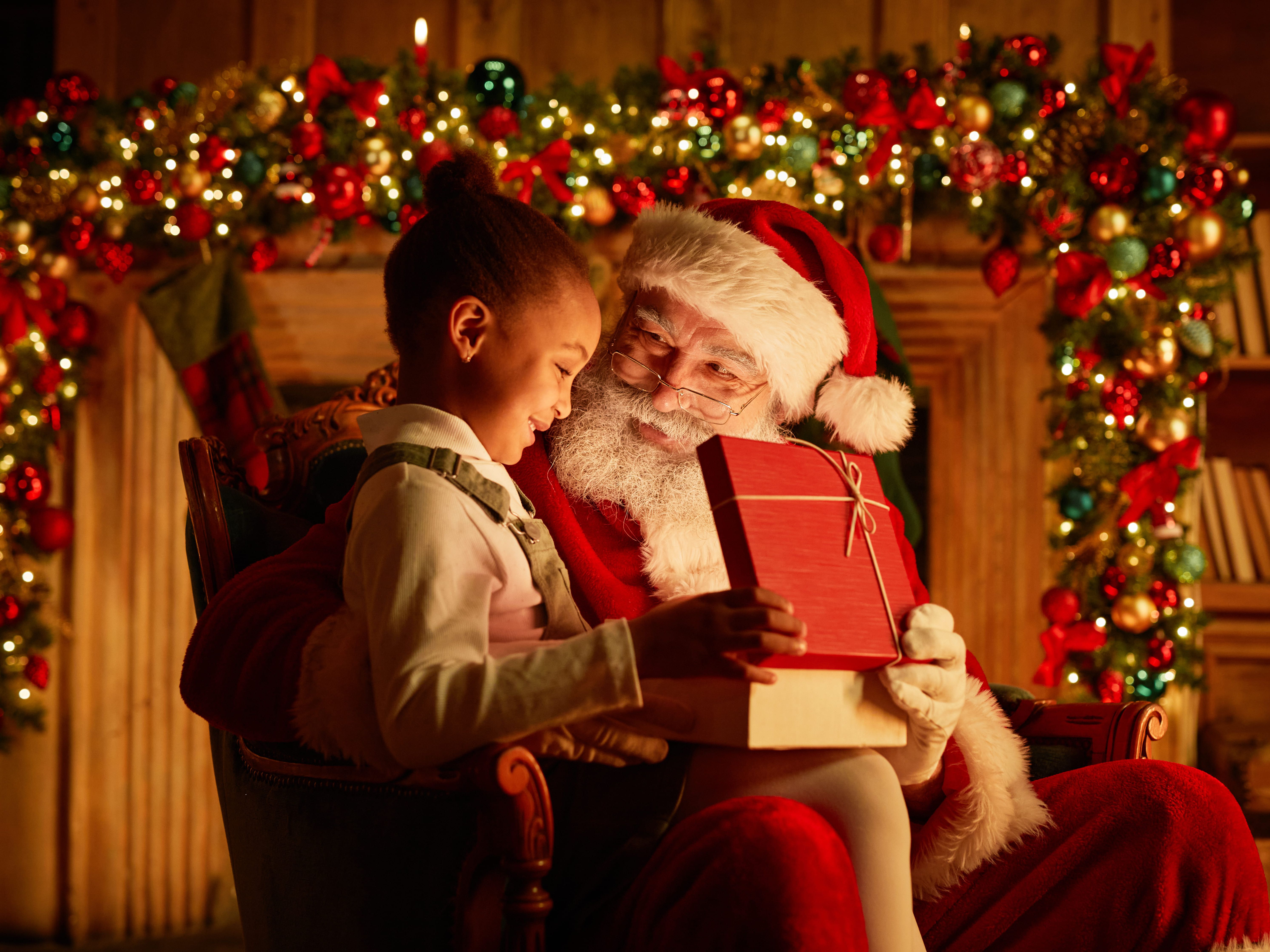 Santa Claus giving a present to a smiling child in front of a decorated Christmas background