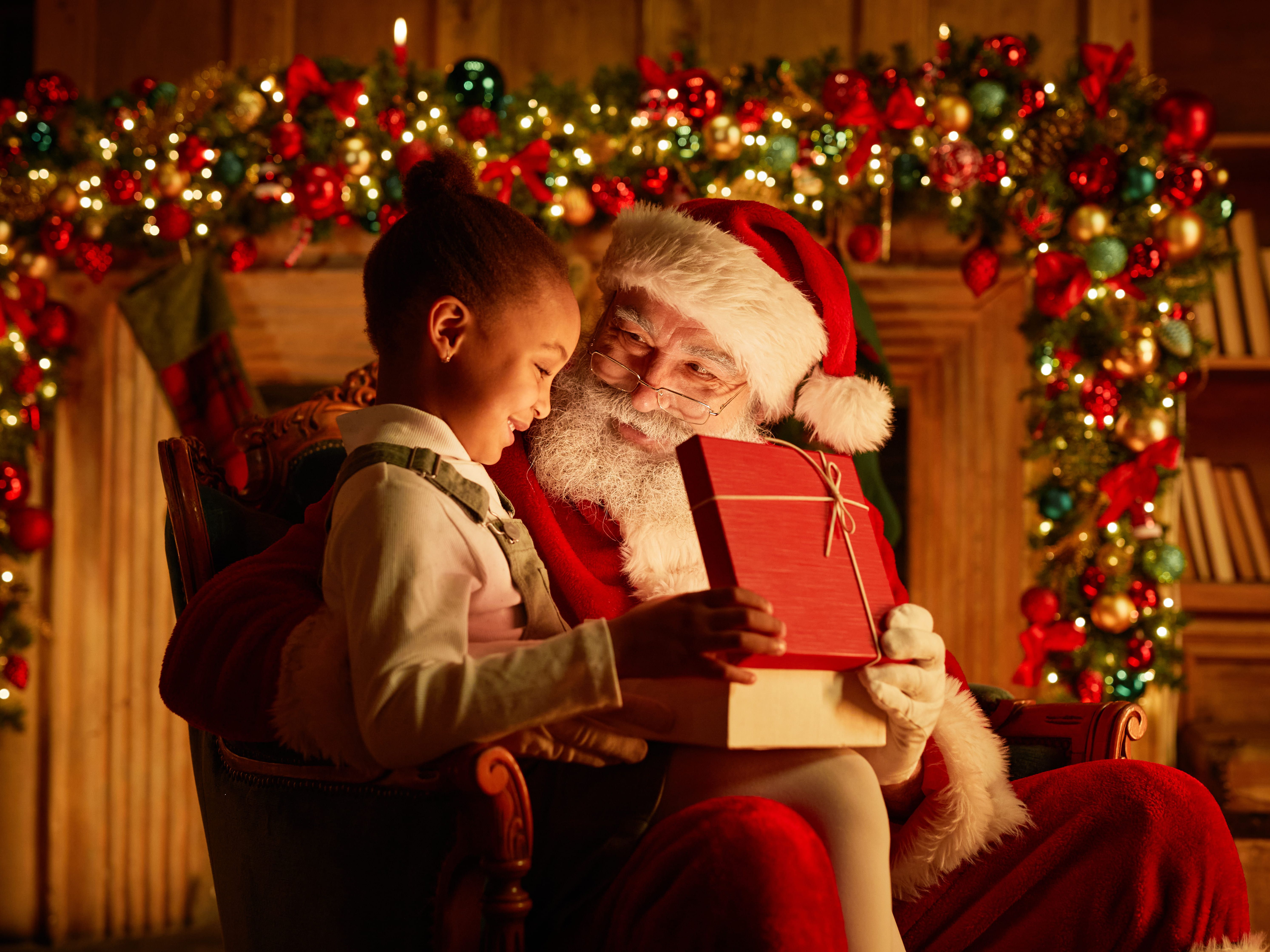 Santa Claus giving a present to a smiling child in front of a decorated Christmas background