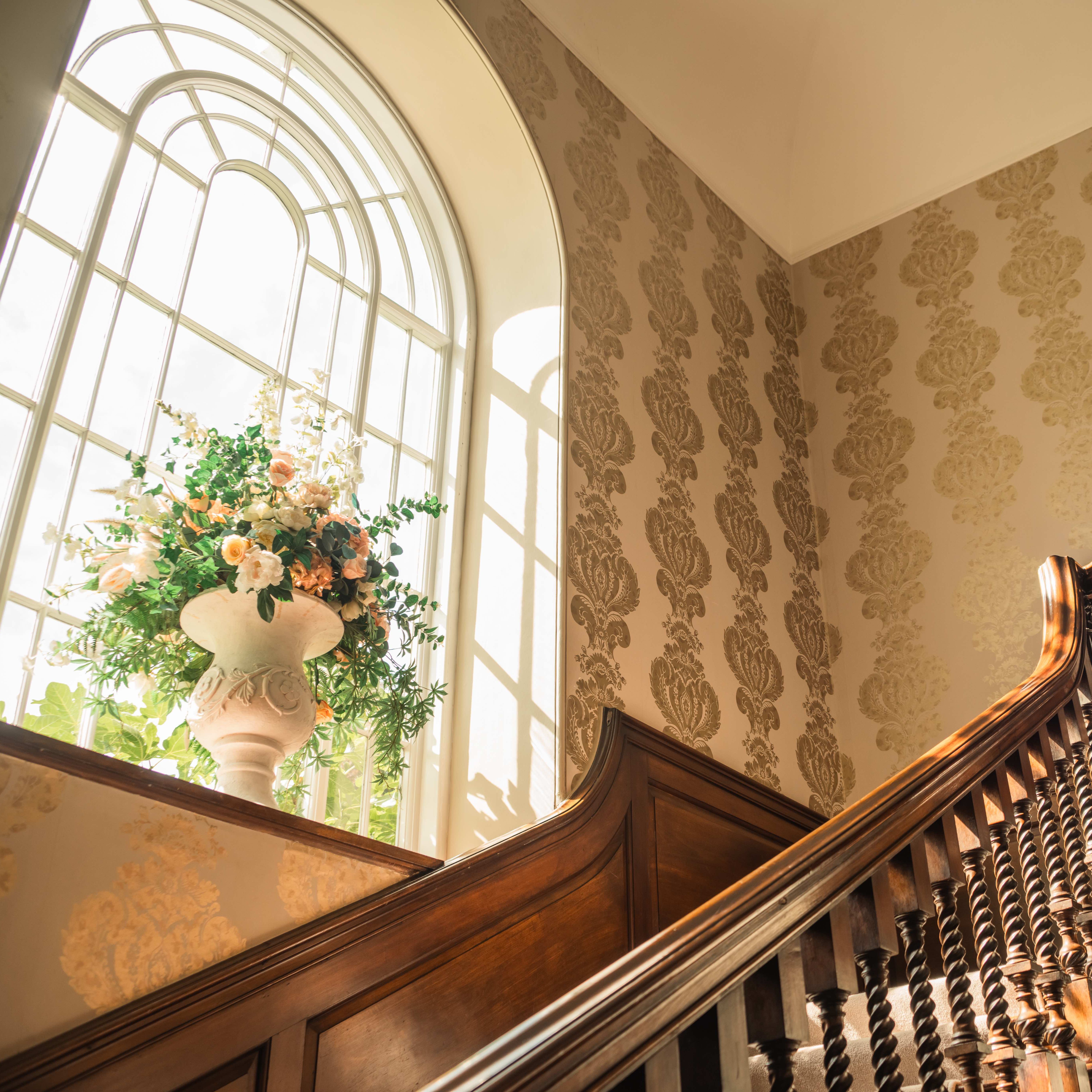 Elegant wooden staircase next to large arched window with floral arrangement