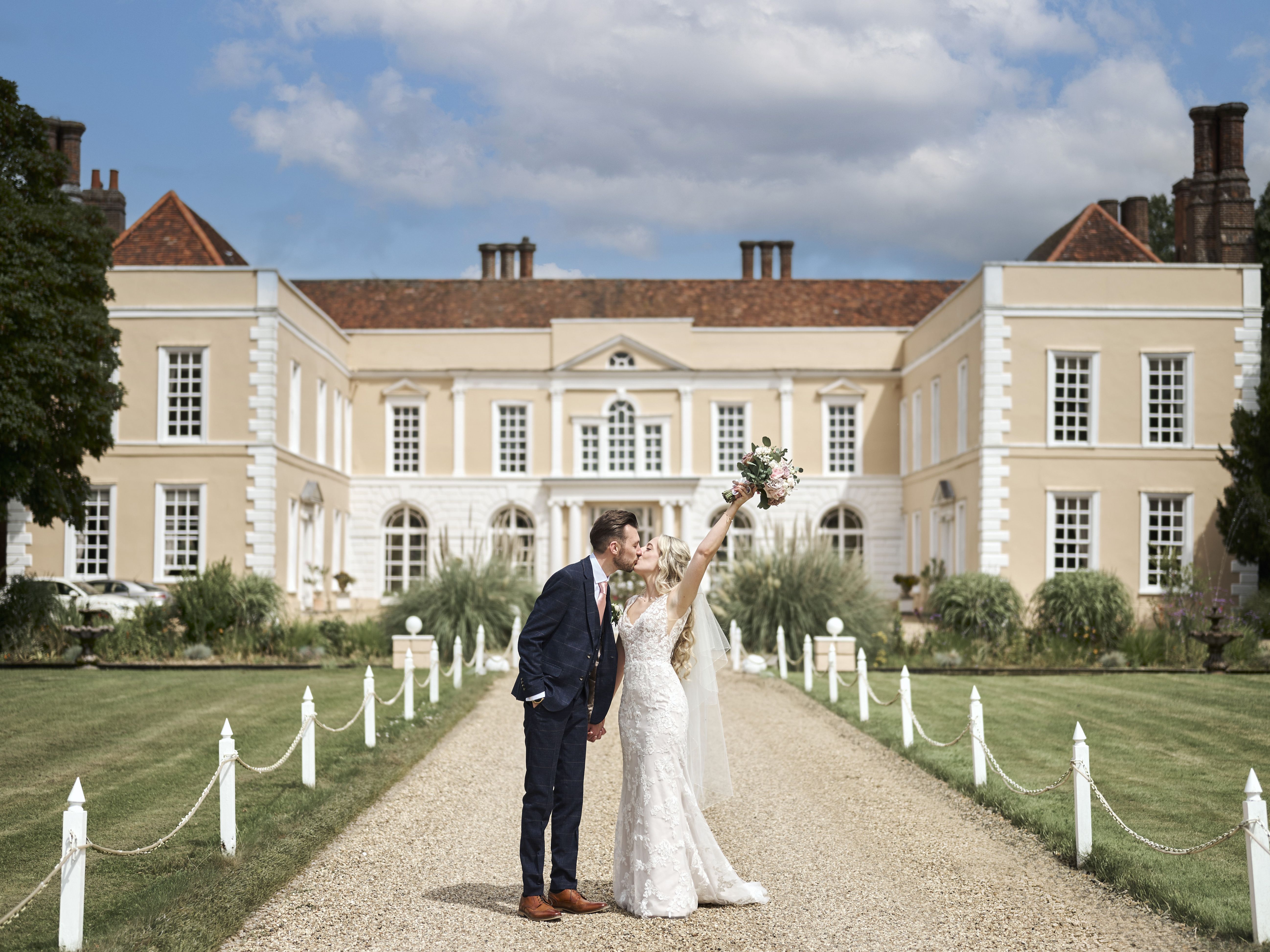Bride and groom kissing outside Hintlesham Hall wedding venue in Ipswich on a sunny day.